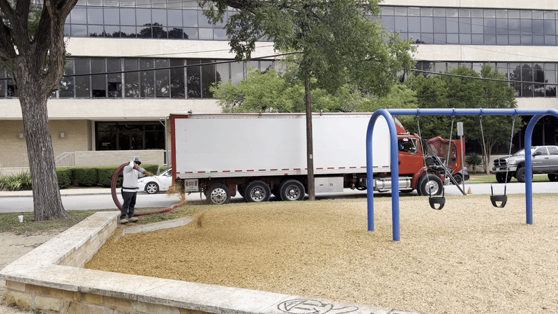 A person sprays high-powered mulch at a swing set.