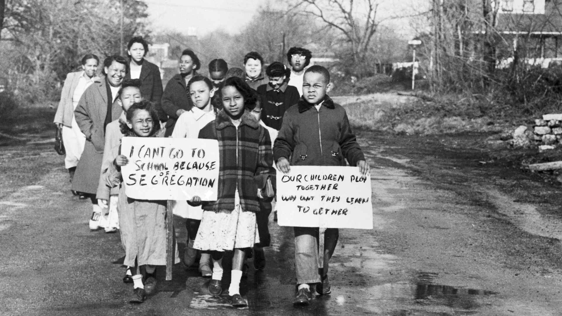 Sixteen Black children accompanied by 4 mothers carry anti-segregation signs as they walk to Webster School in Hillsboro, Ohio, in 1956.
