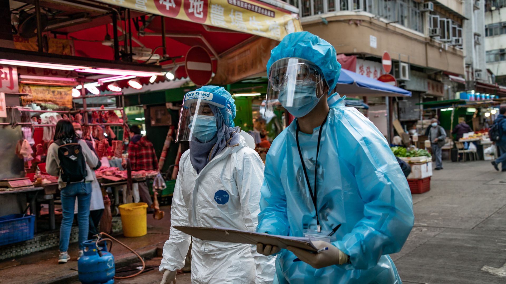 Photo of two health care workers in hazmat suits walking around a neighborhood in Hong Kong