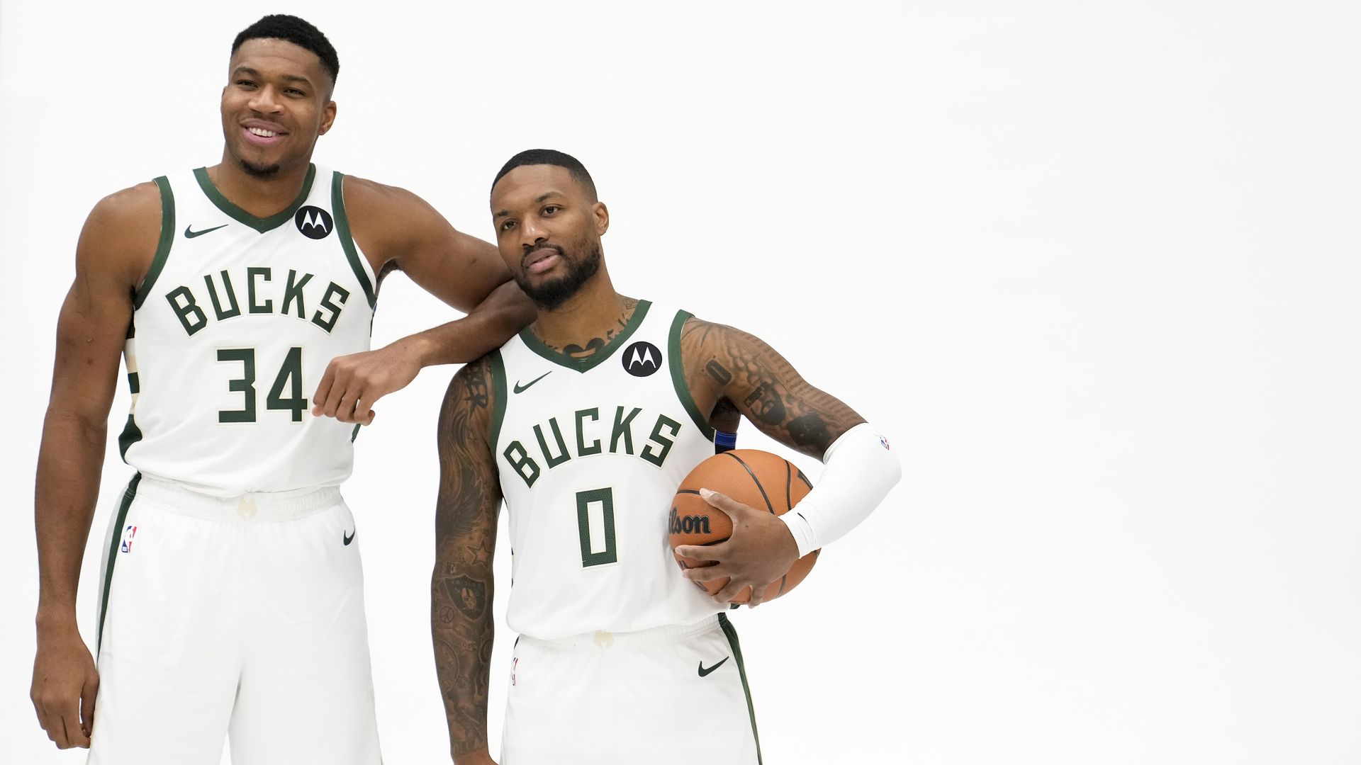 Giannis Antetokounmpo and Damian Lillard in white Bucks uniforms against a white backdrop