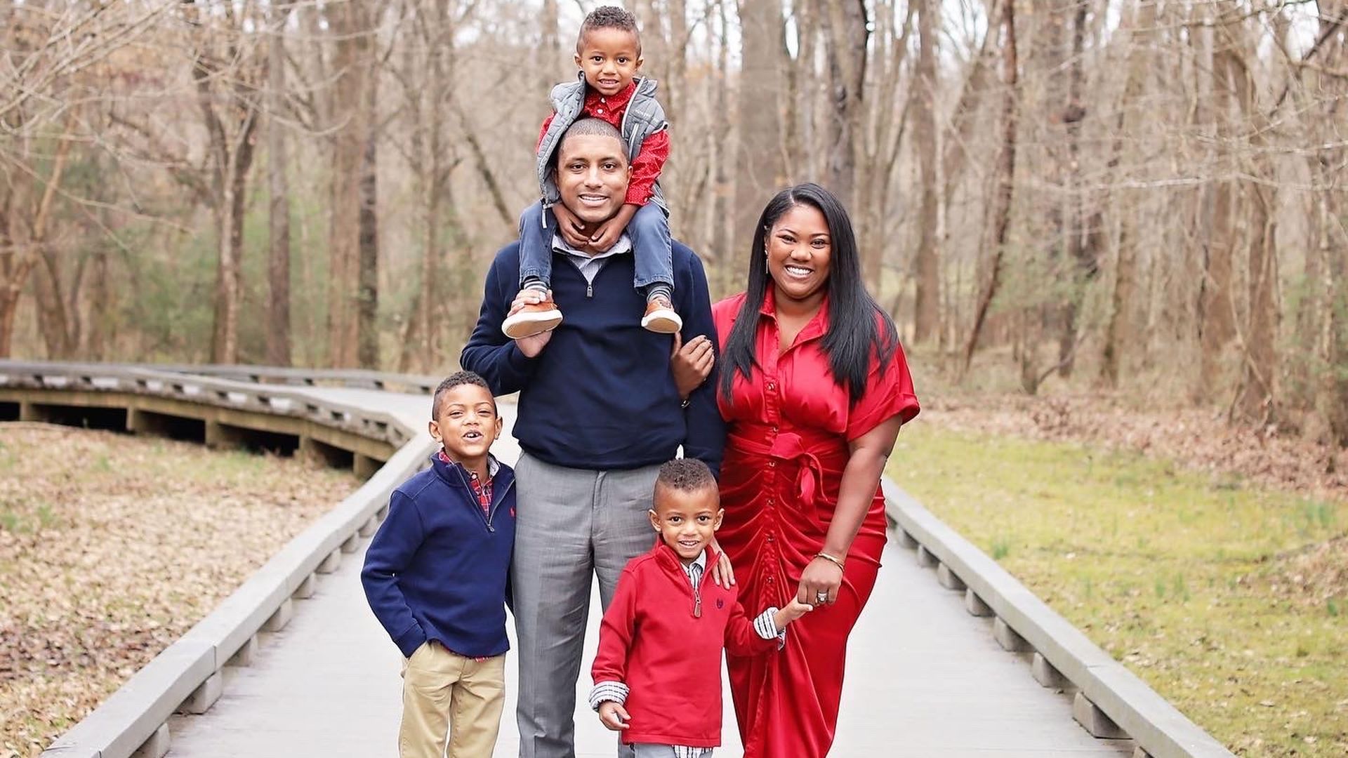 Justin Harlow stands in the woods with three children, one on his shoulder, and his wife Kiara.