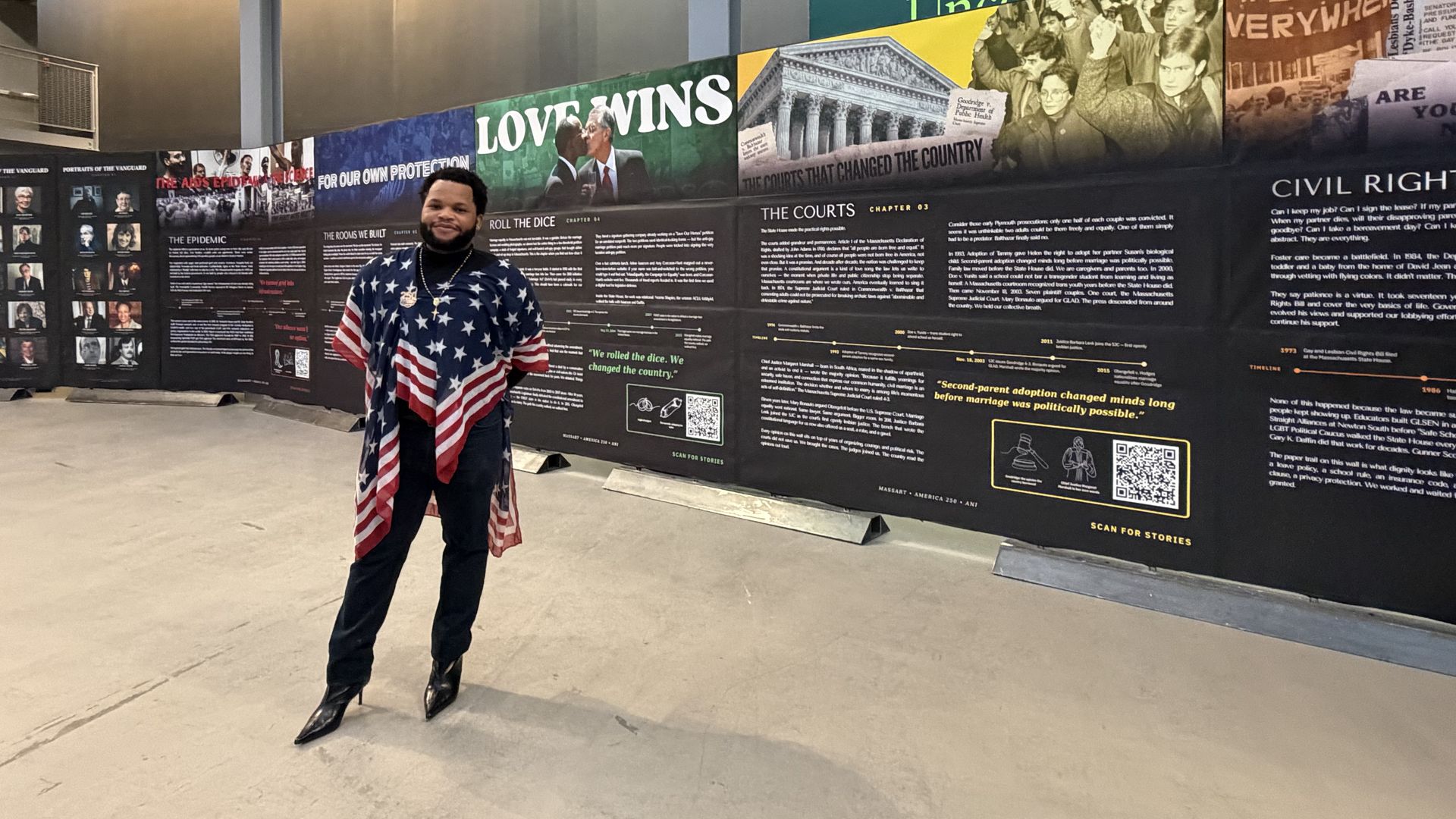 Jean Dolin, founder of the Boston LGBTQ+ Museum, wears a shawl with the design of the USA flag, as he stands in front of the new LGBTQ+ history display, "Portraits of The Vanguard" inside the MassArt Museum in Boston on July 30, 2026.