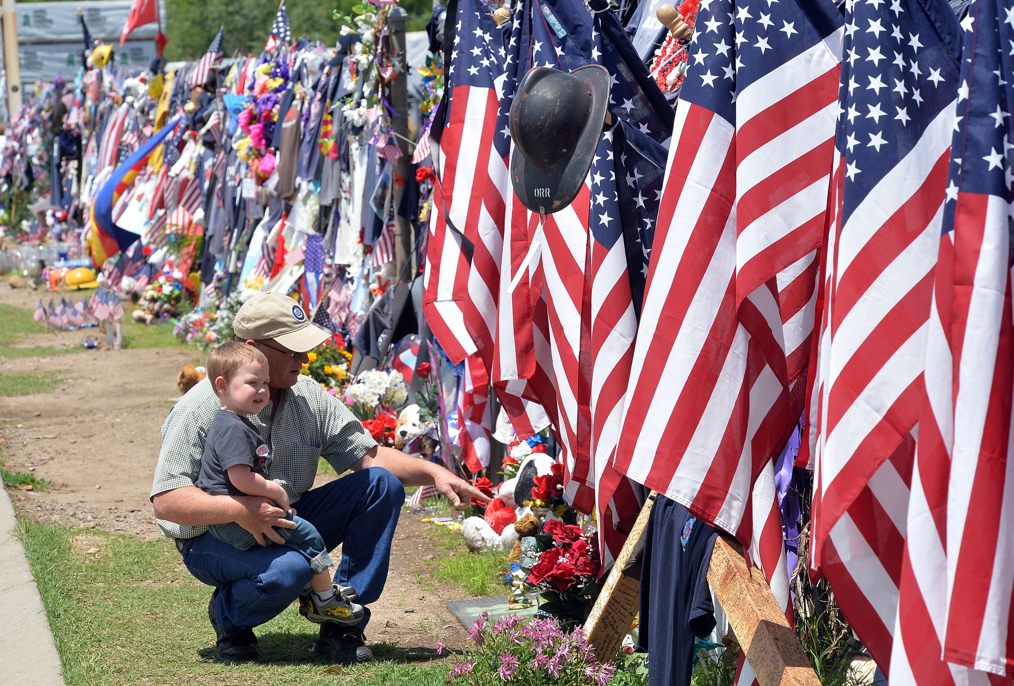 A man and his son looking at a fence covered in American flags and other items. 