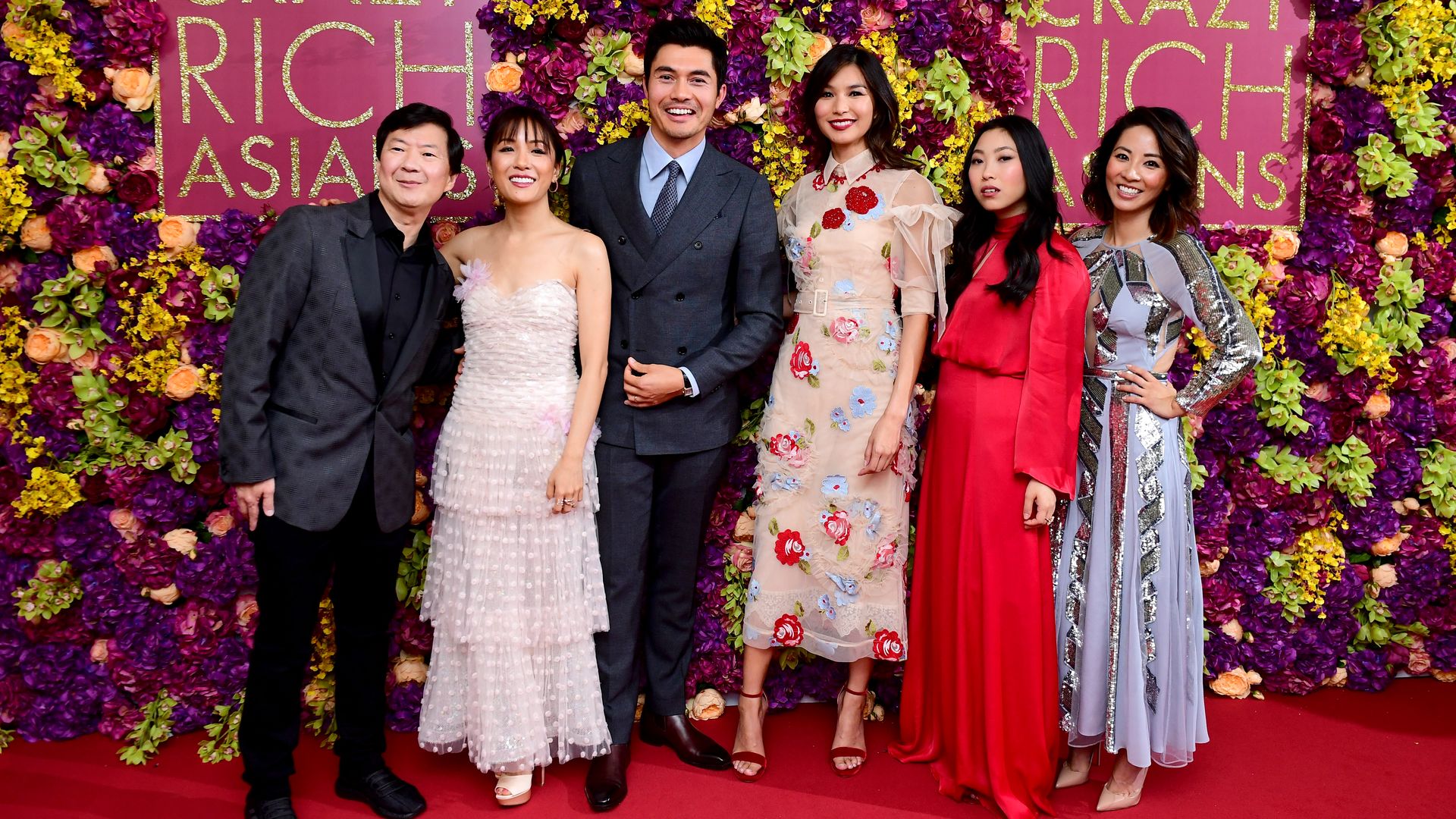 Actors Ken Jeong, Constance Wu, Henry Golding, Gemma Chan, Awkwafina and Jing Lusi stand in front of a floral wall at the "Crazy Rich Asians"movie premiere. 