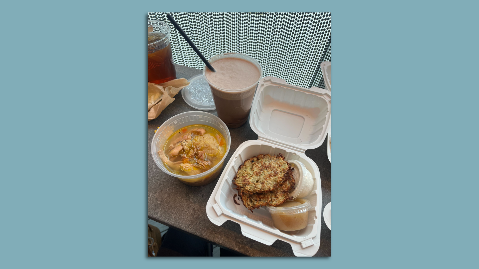 A photo of matzo soup in a to-go container and latkes with apple sauce and cream.