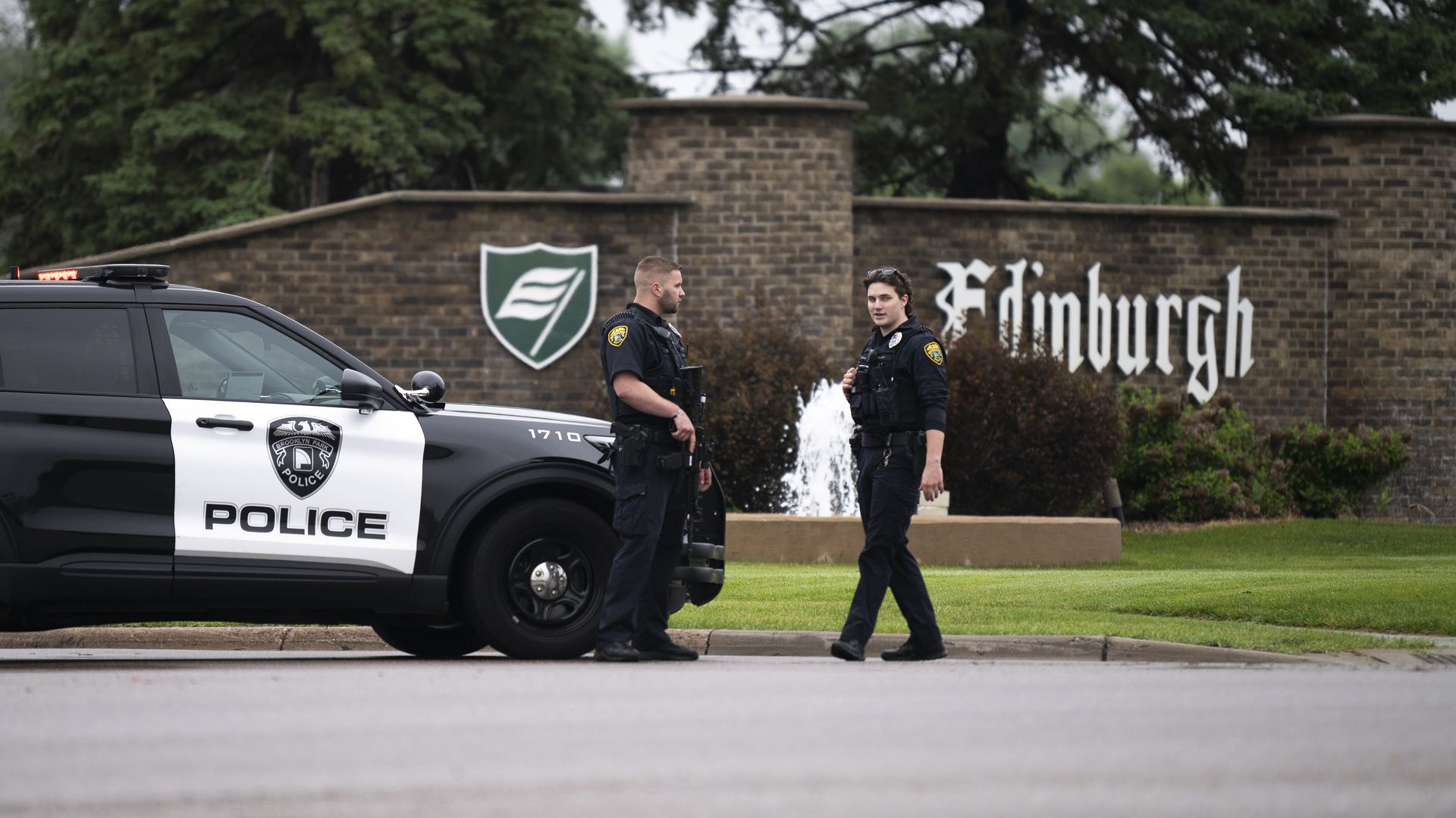 Two police officers speak while patroling a street in front of a sign that says "Edinburgh" the name of a nearby golf course