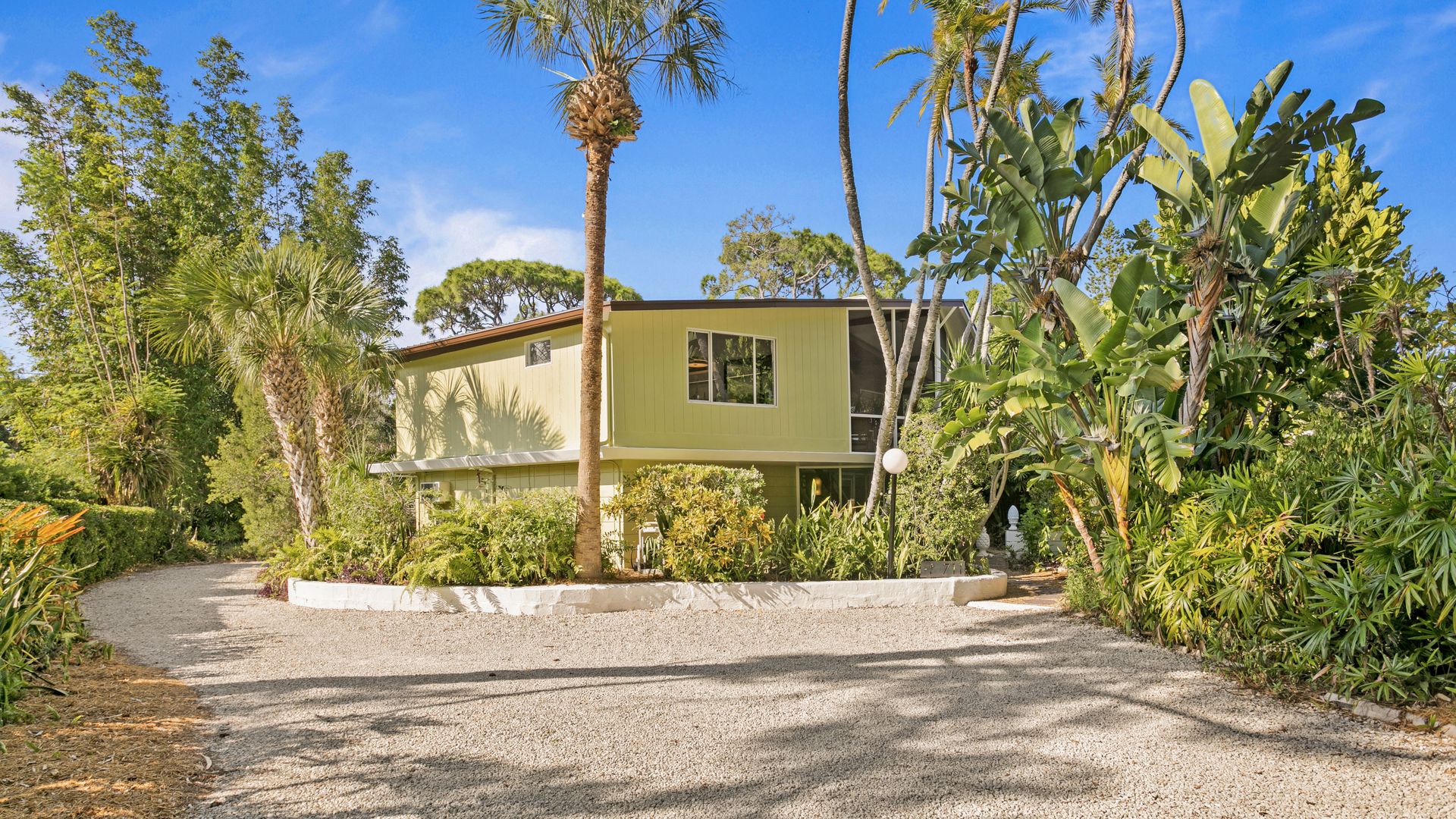A pale-green mid-century style home surrounded by tropical landscaping.