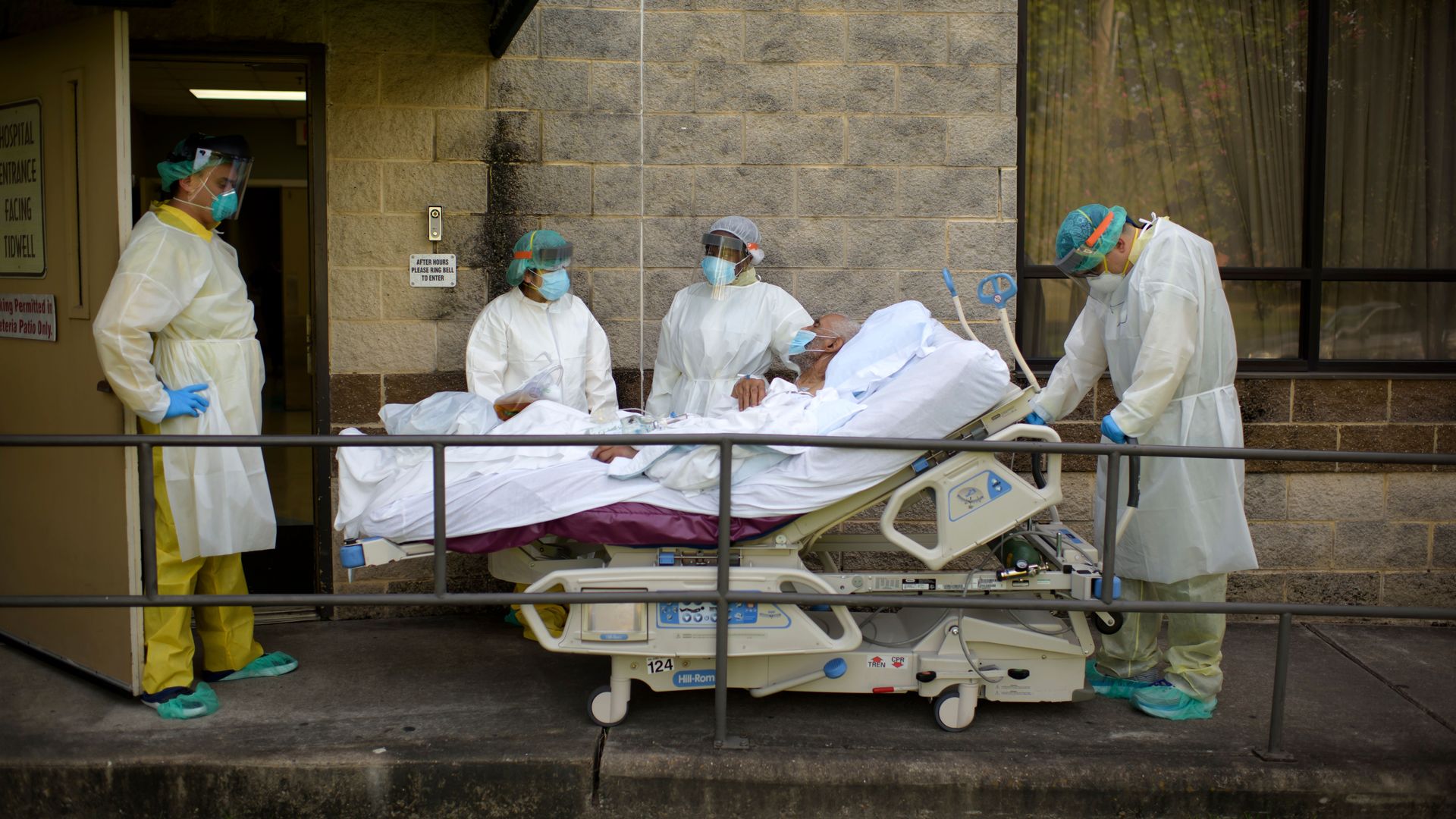 A coronavirus patient is wheeled in a hospital bed by workers in masks and gowns.
