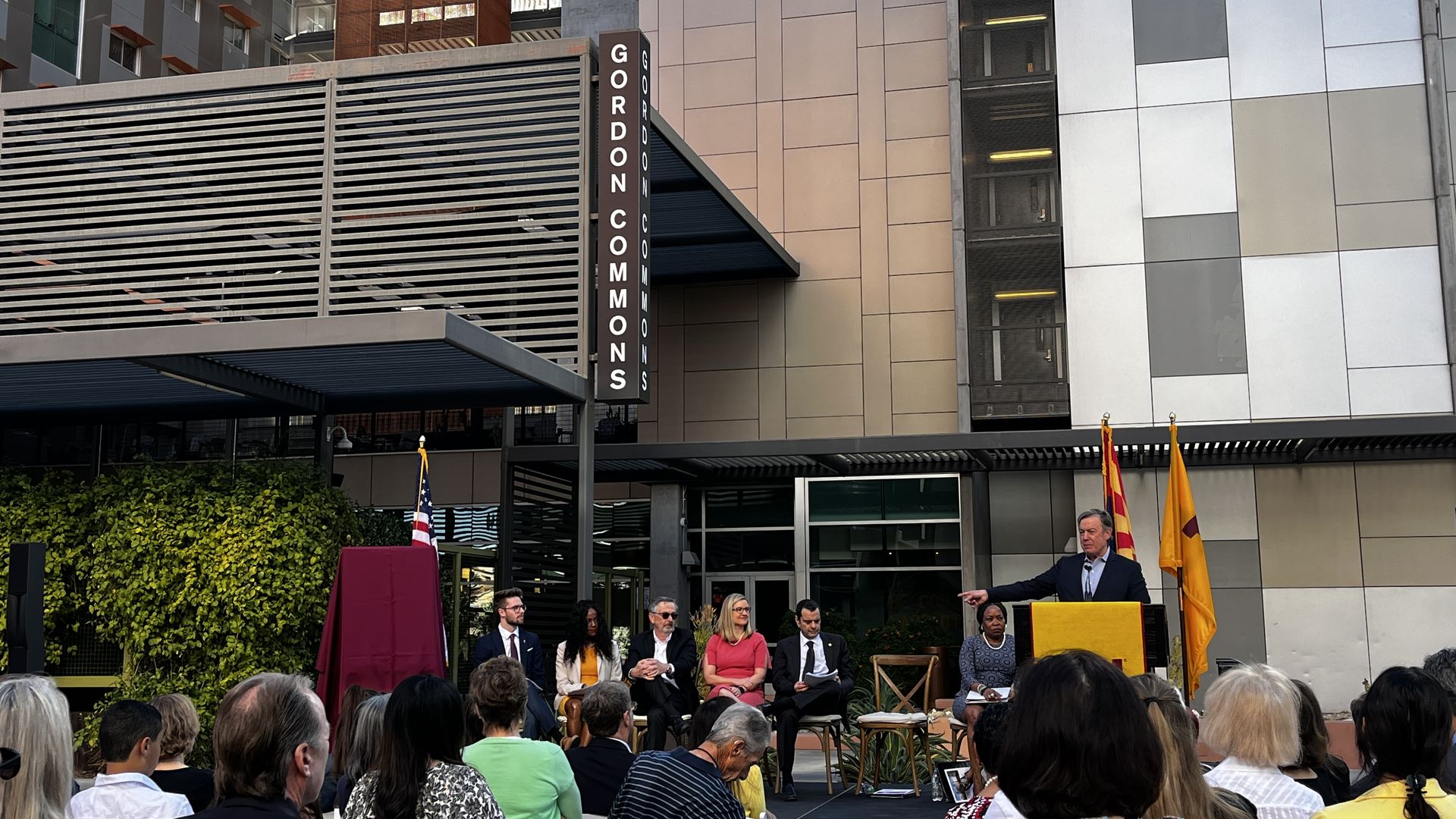 A group of people sitting on a stage outside a building that says, "Gordon Commons."