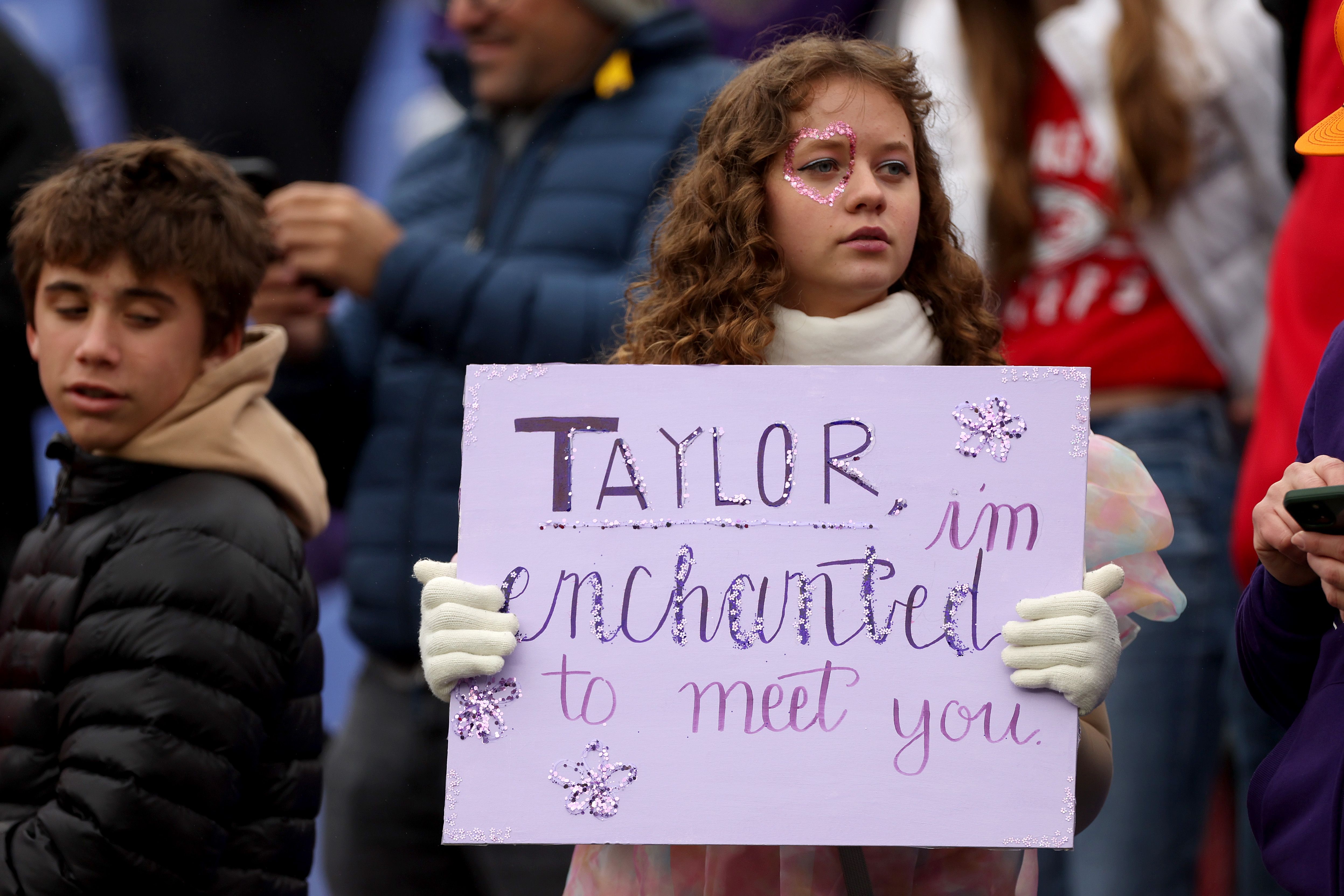 A child in the stadium stands holds up a sign that says "Taylor, I'm enchanted to meet you."