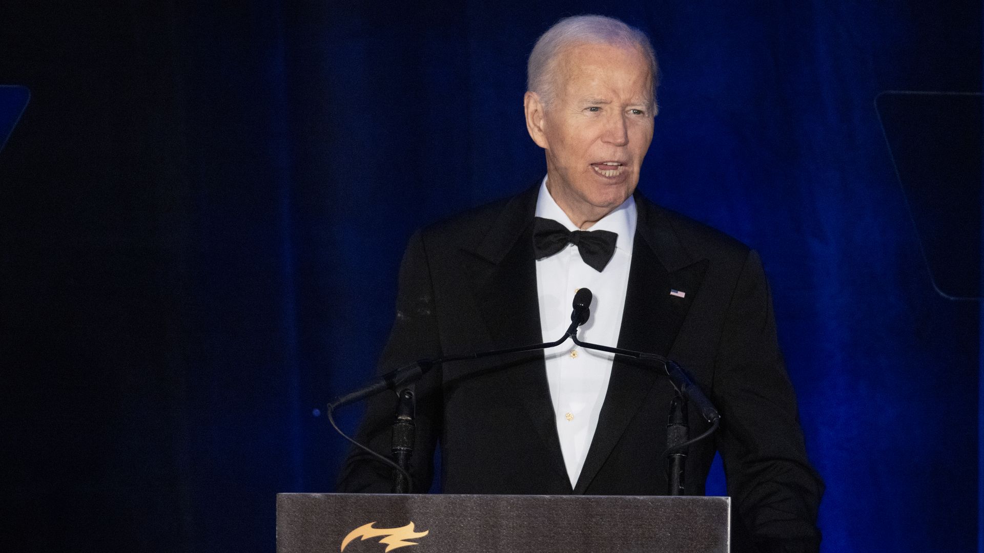 Former President Biden, wearing a black tuxedo and white shirt, speaking at a podium with a sign saying "The National Bar Association 100 years."