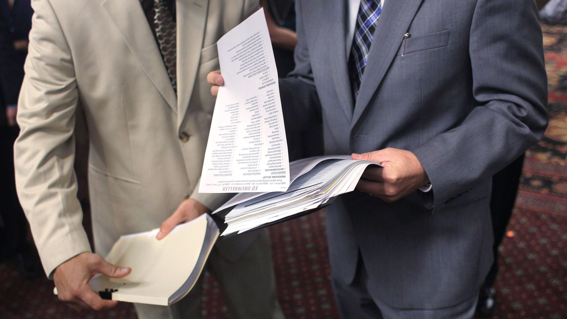 Two people in suits flip through job offerings at career fair.
