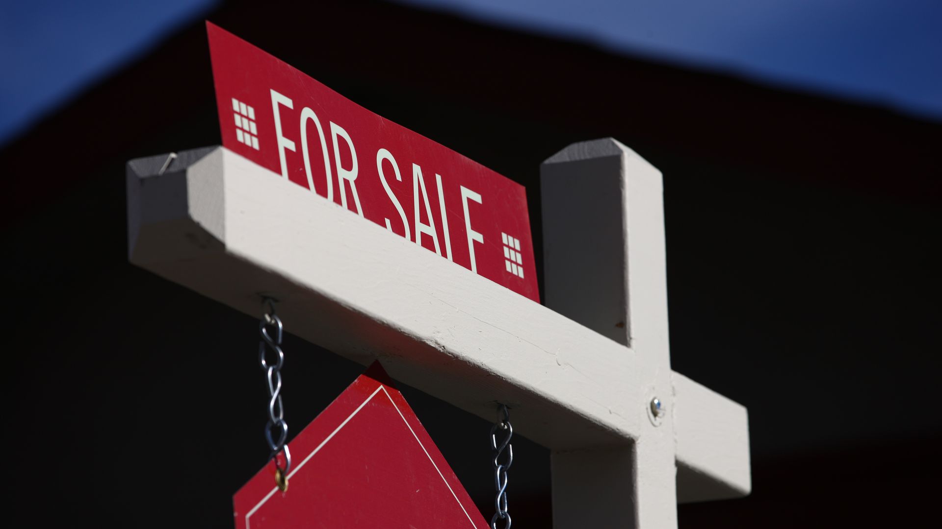 A photo of a red "for sale" sign hanging in front of a house.