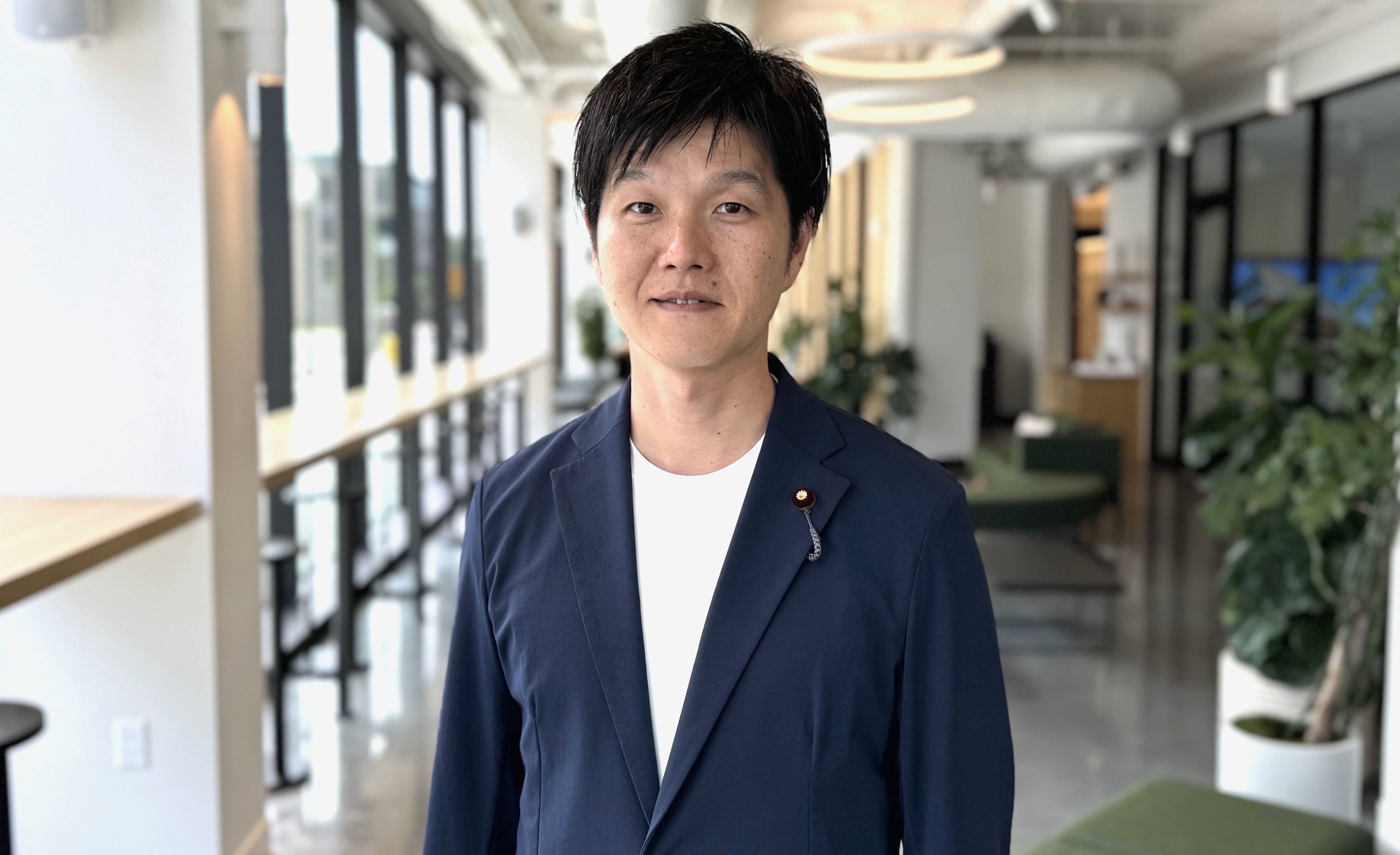 A photo of a man in a suit jacket standing in a business office hallway.