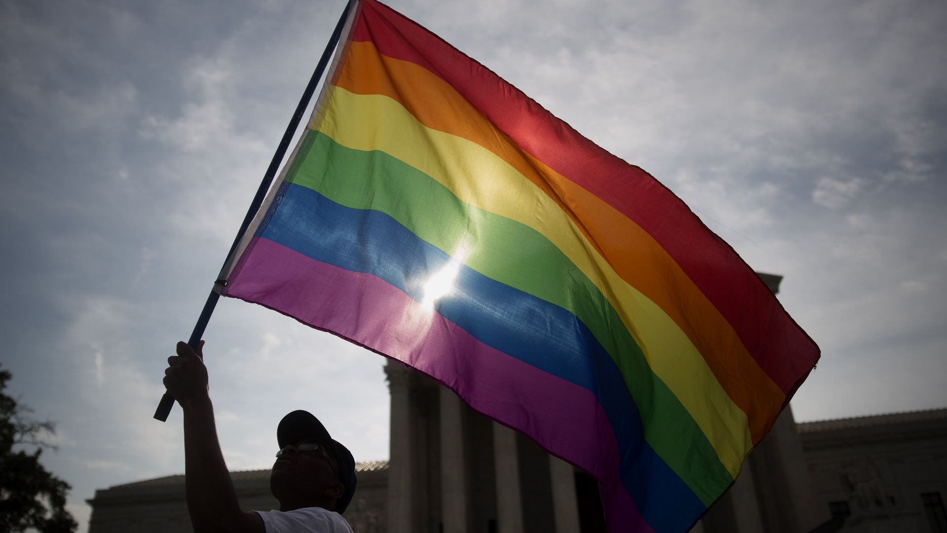 Photo of a silhouetted person waving a rainbow flag in front of the Supreme Court building