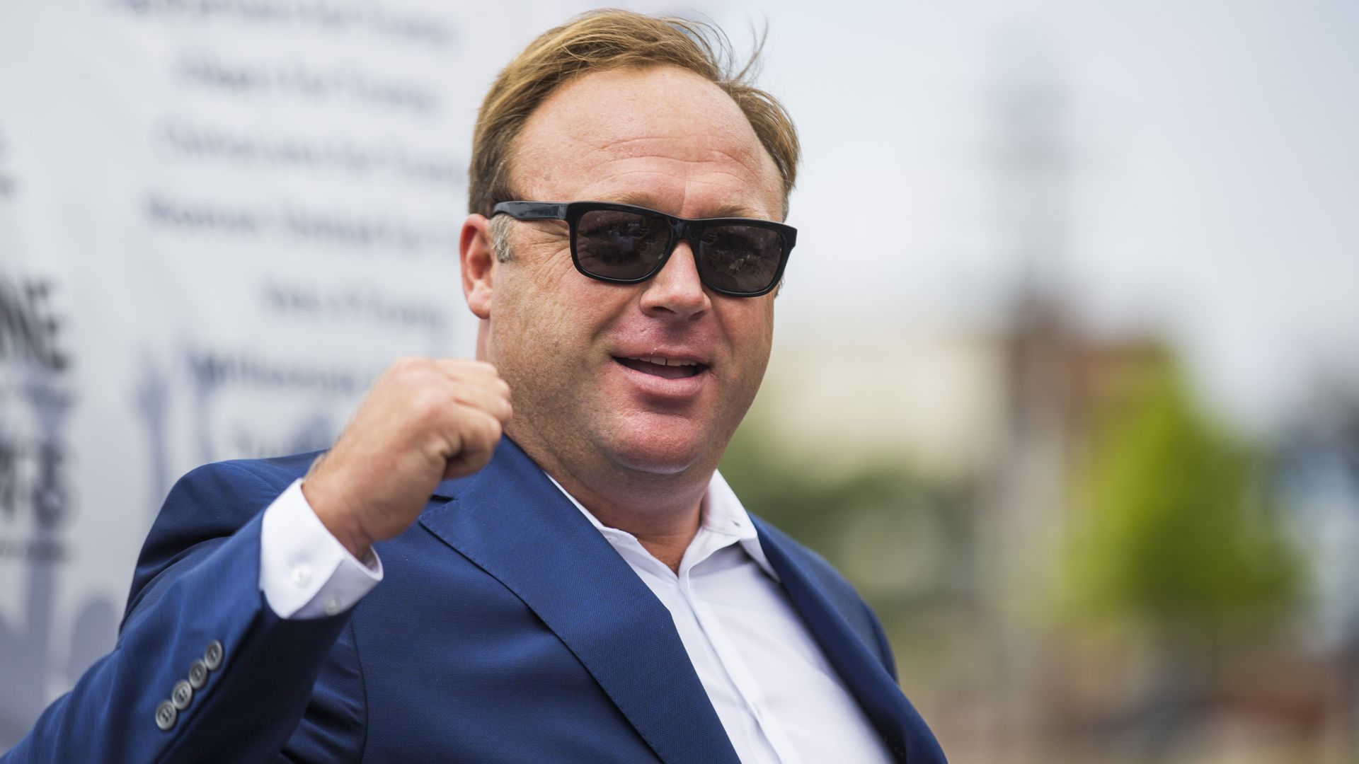 Alex Jones wearing a blue suit and sun glasses.