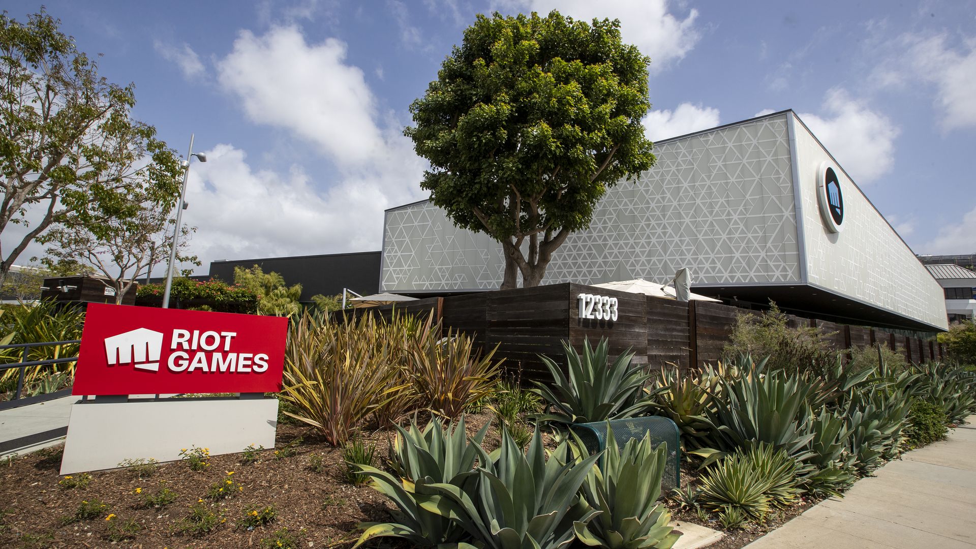 Photo of a building flanked by palm trees. A red sign nearby bears the logo for Riot Games