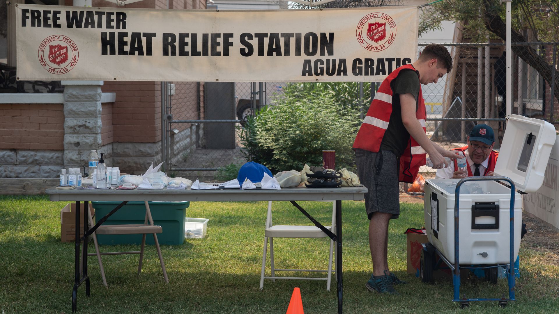 A man putting water in a cooler under a sign that says "Heat Relief Station."