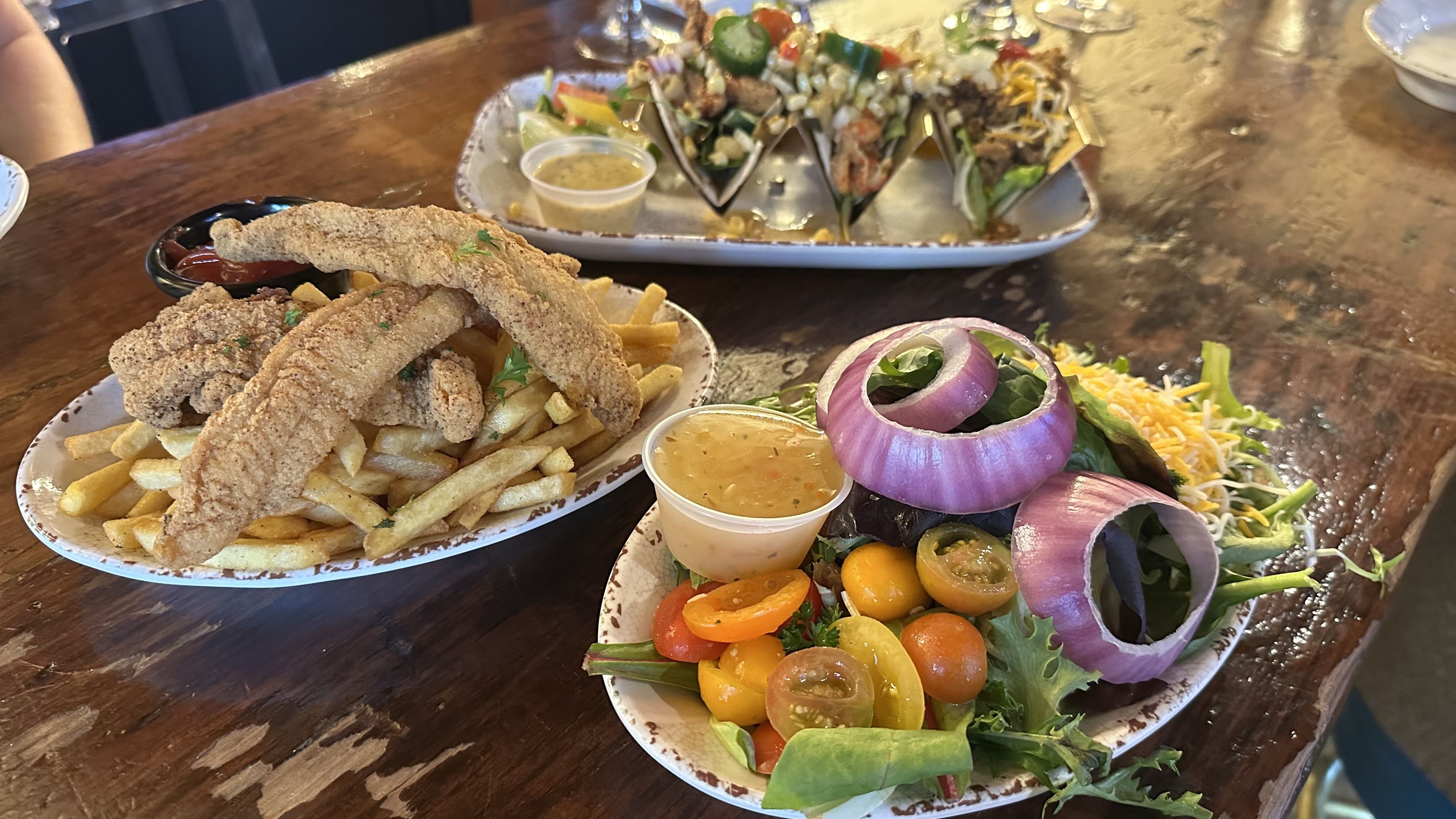 A photo of a fish plate, salad and three tacos.