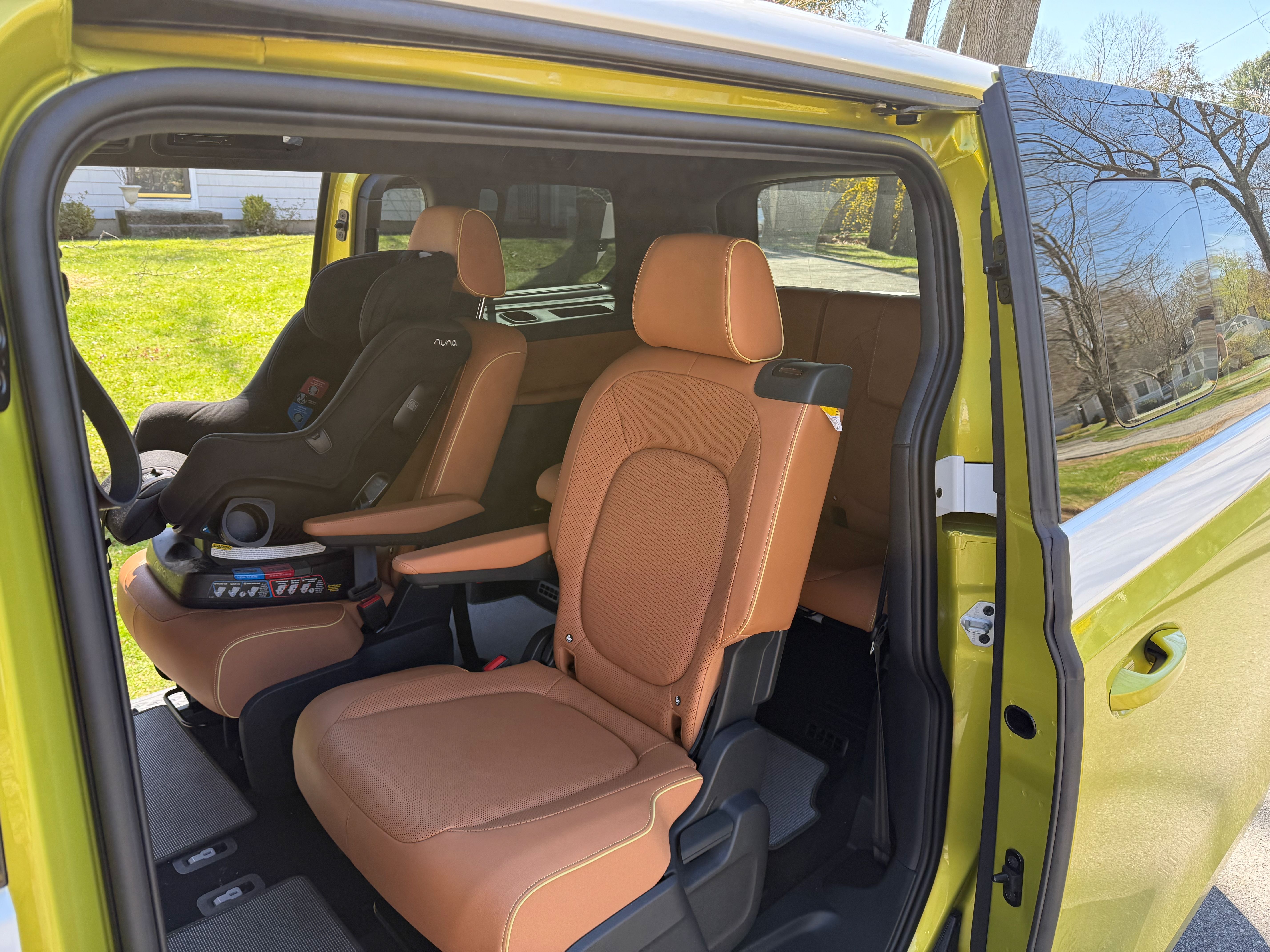 A photo of the brown-leather second and third rows of the VW ID.Buzz minivan, with both sliding doors open, and a black child seat on one of the second-row captain's chairs.