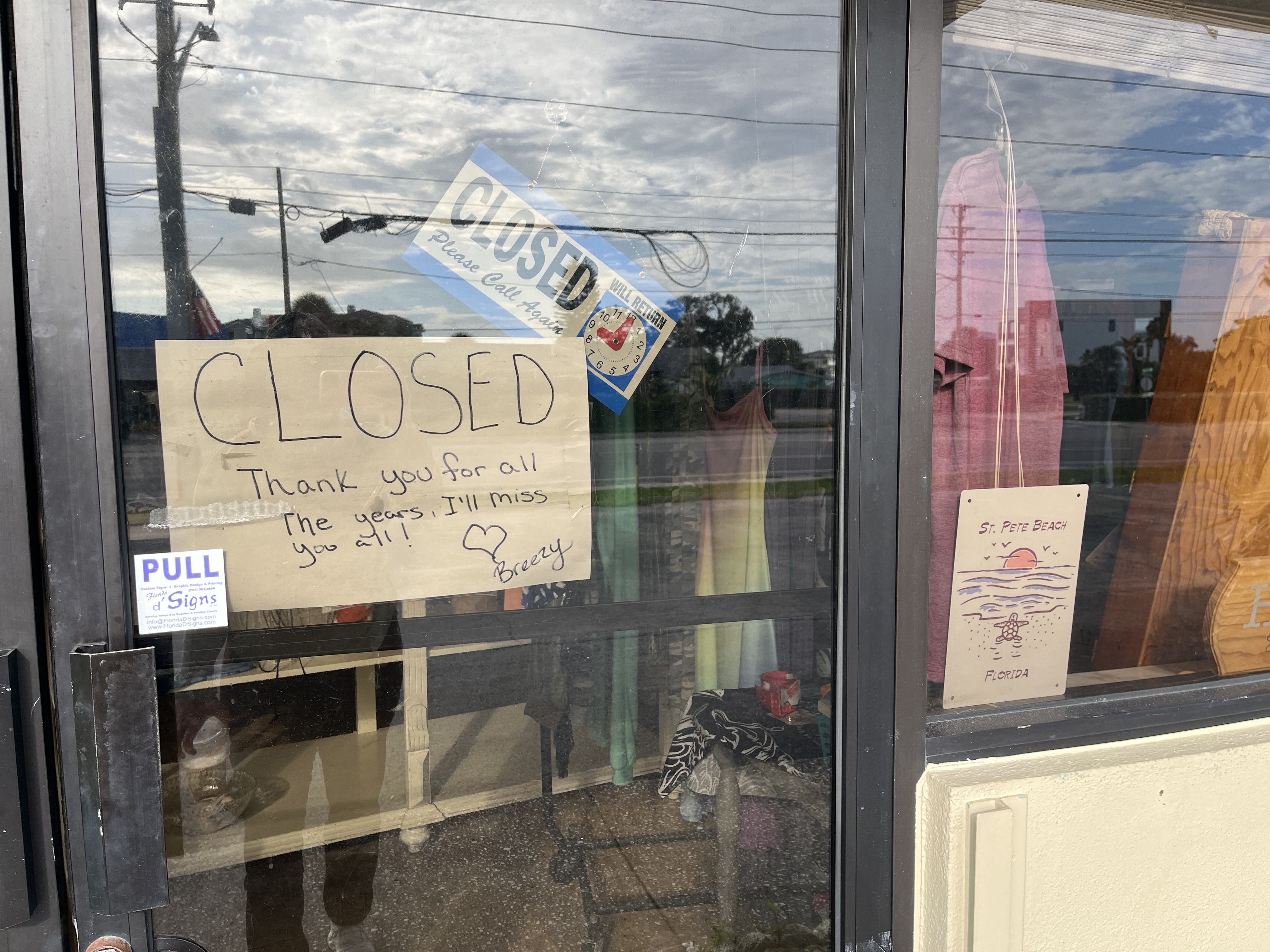 A closed store door with handwritten sign saying "CLOSED Thank you for all the years. I'll miss you all!" signed Breezy, a printed "CLOSED" sign, and a postcard reading "St. Pete Beach Florida."