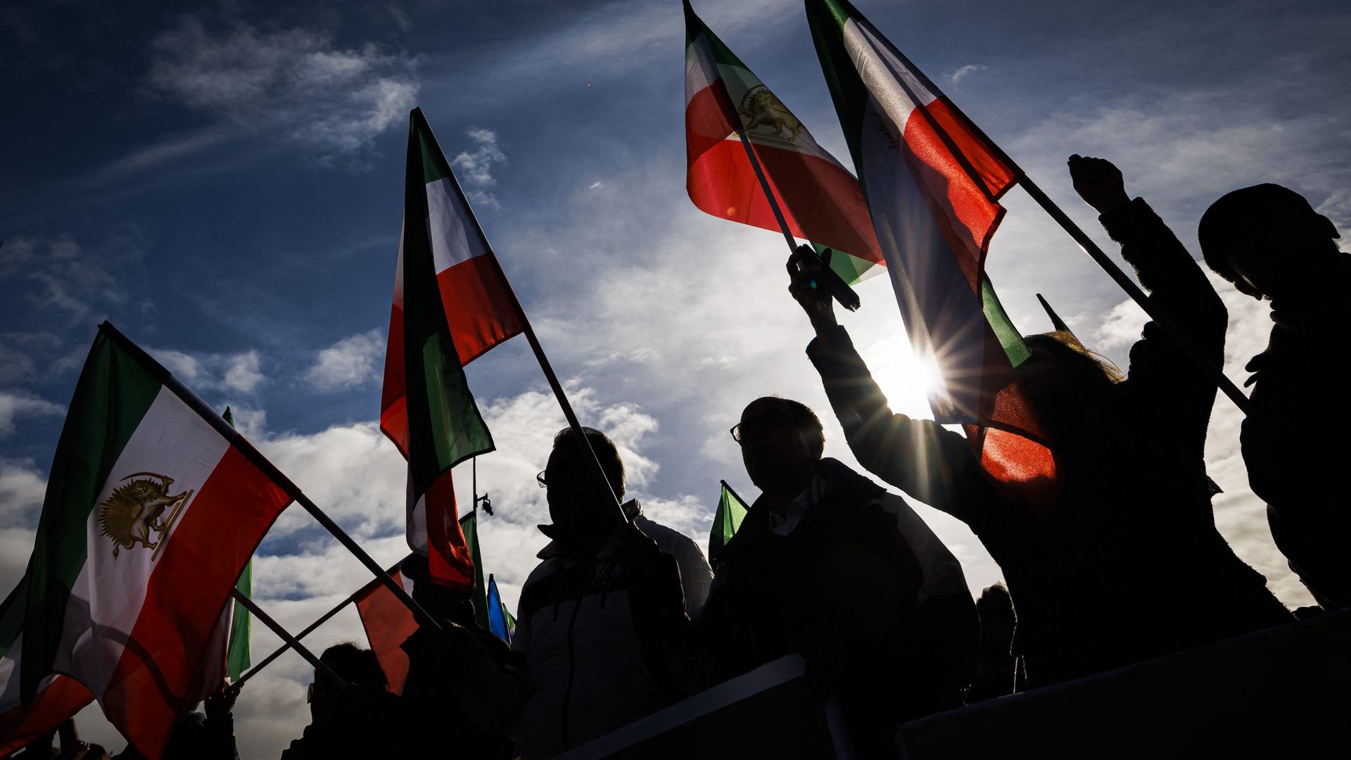 Photo of people silhouettes as the raise Iranian pre-Islamic flags in the air at a protest