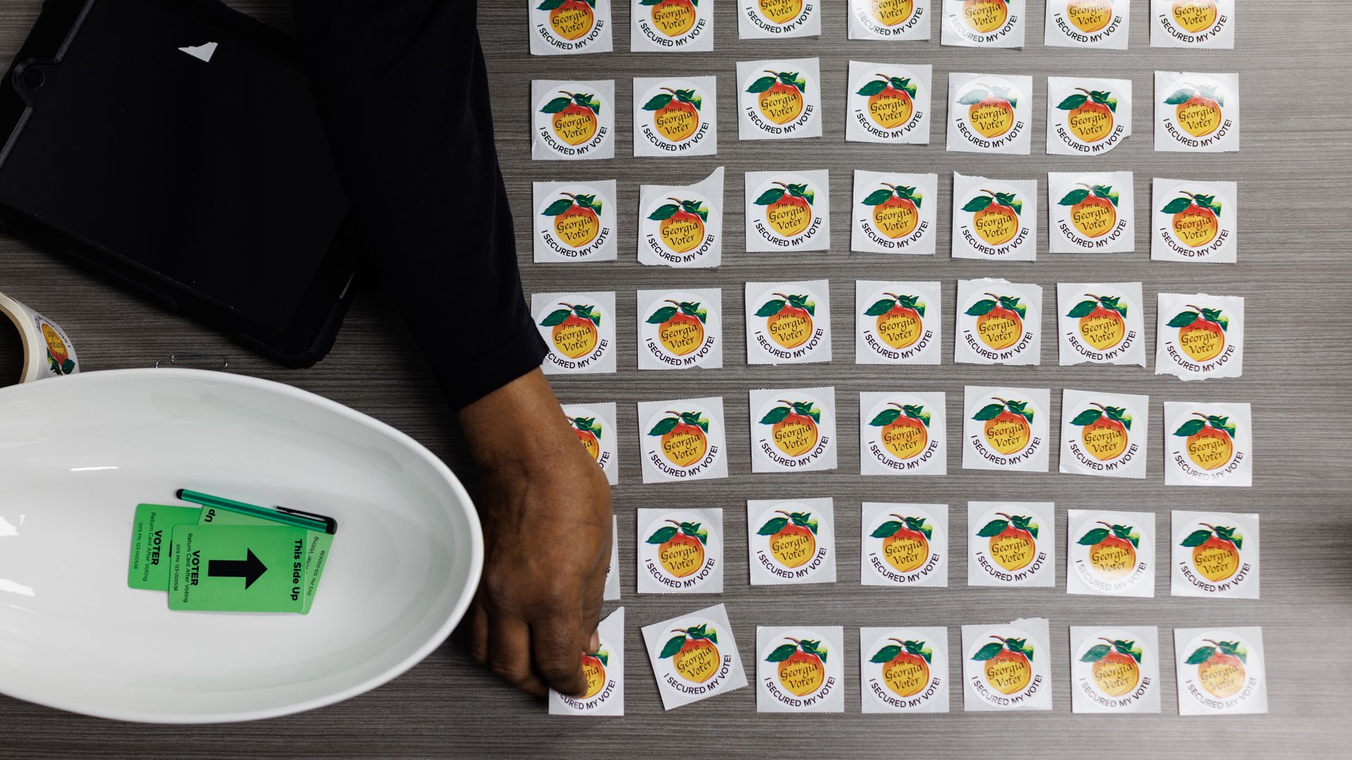 A photo taken from above of a poll worker's hand laying out "I voted" stickers given to Georgia voters