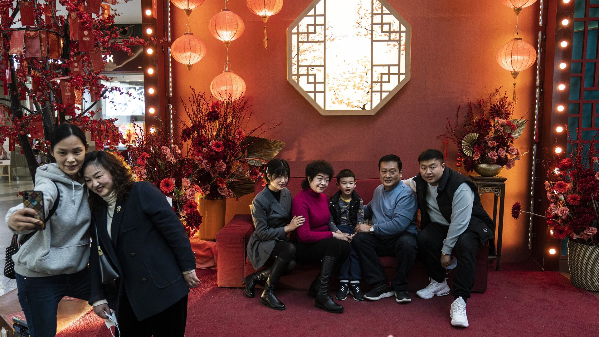 Two women takes a selfie as a family poses for pictures in a Shopping Mall during the fifth day of Spring Festival on February 16, 2021 in Wuhan