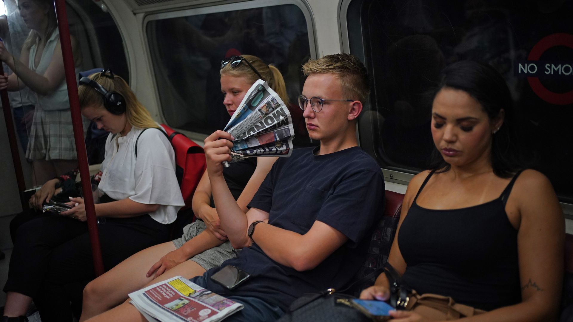 Man on London subway fans himself with newspaper during a heat wave.