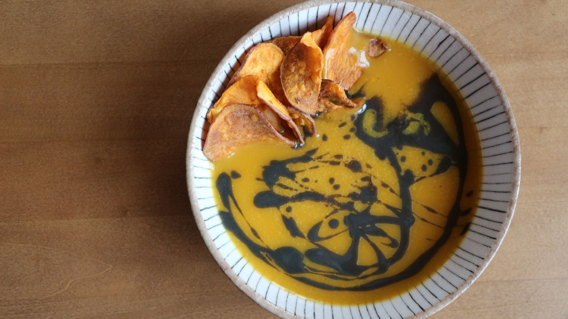 A bowl of soup topped with an oil drizzle and potato chips.