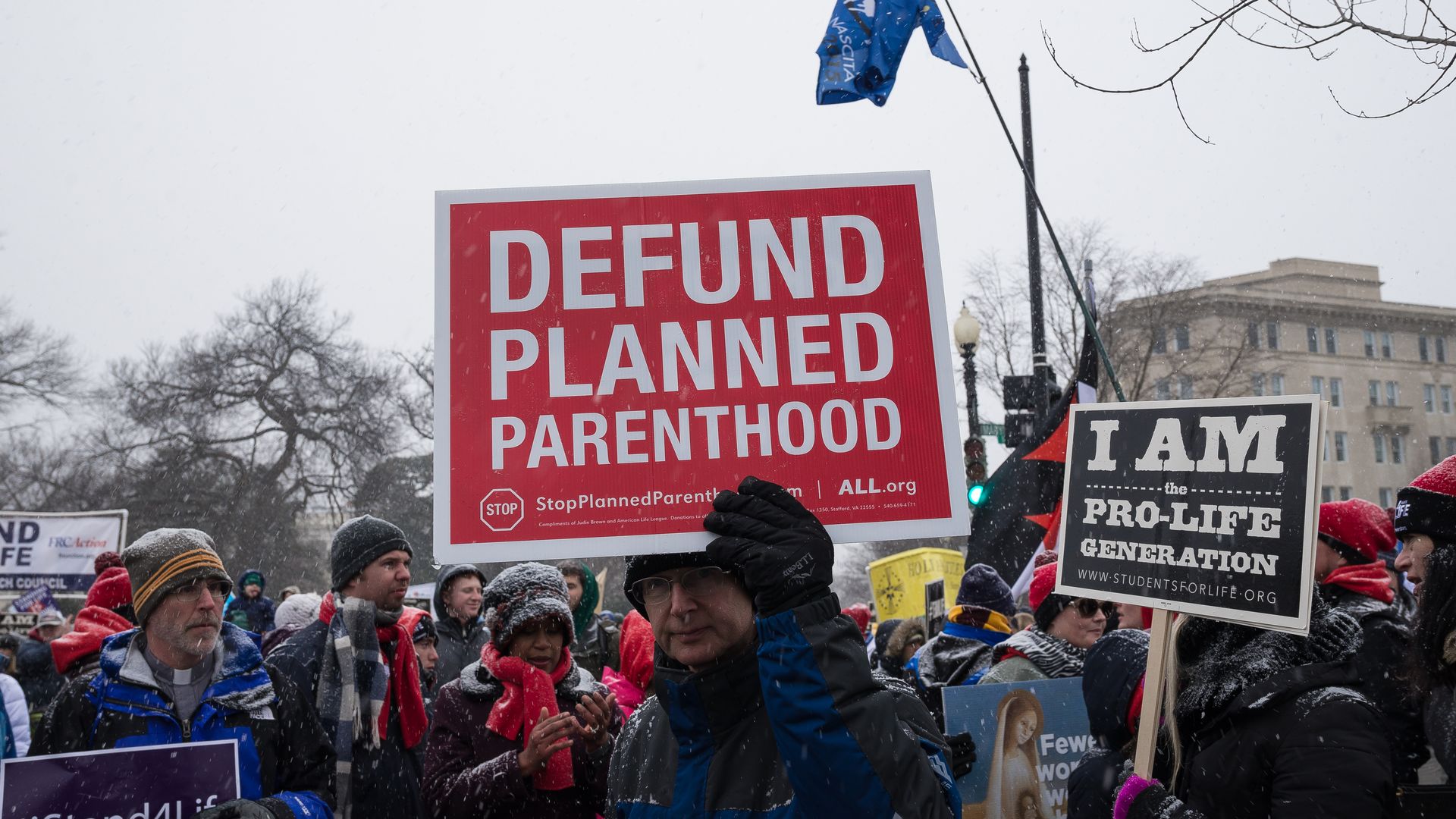 A man holds a "Defund Planned Parenthood" sign