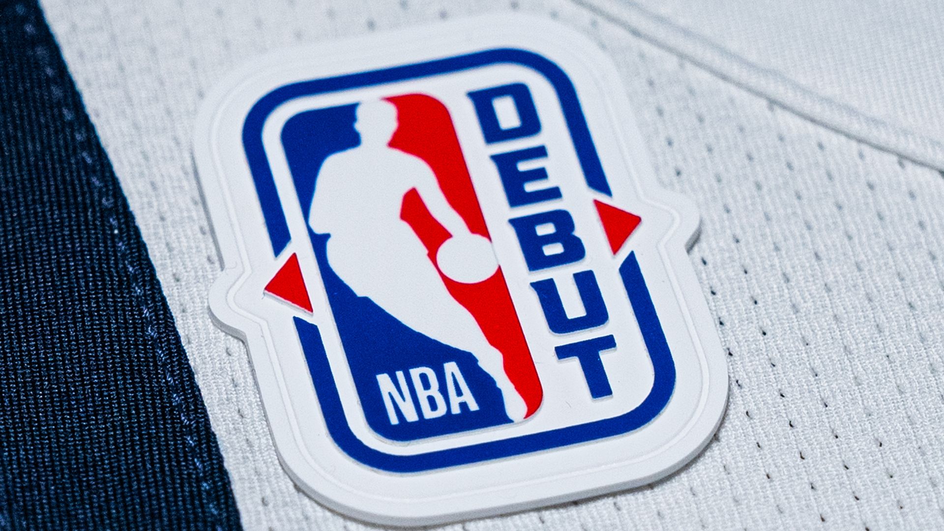 Close-up of a white and blue NBA jersey with an NBA logo patch featuring a silhouette and the word DEBUT, alongside a blue Nike swoosh and a red Topps logo.