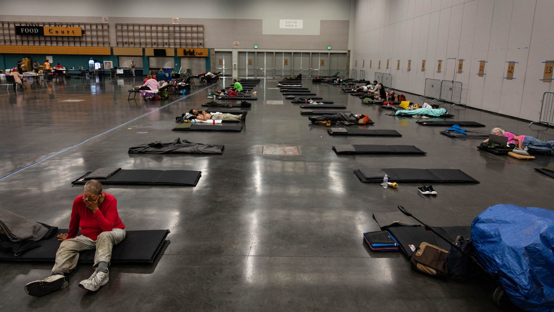 People sitting on matts in a large room, seeking cooler air during a heat wave in Portland, Oregon.