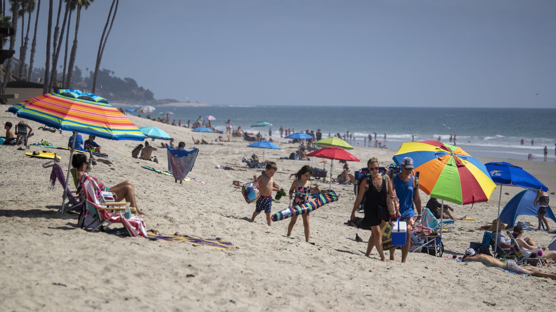 People sit on a beach under colorful umbrellas and walk on the sand 