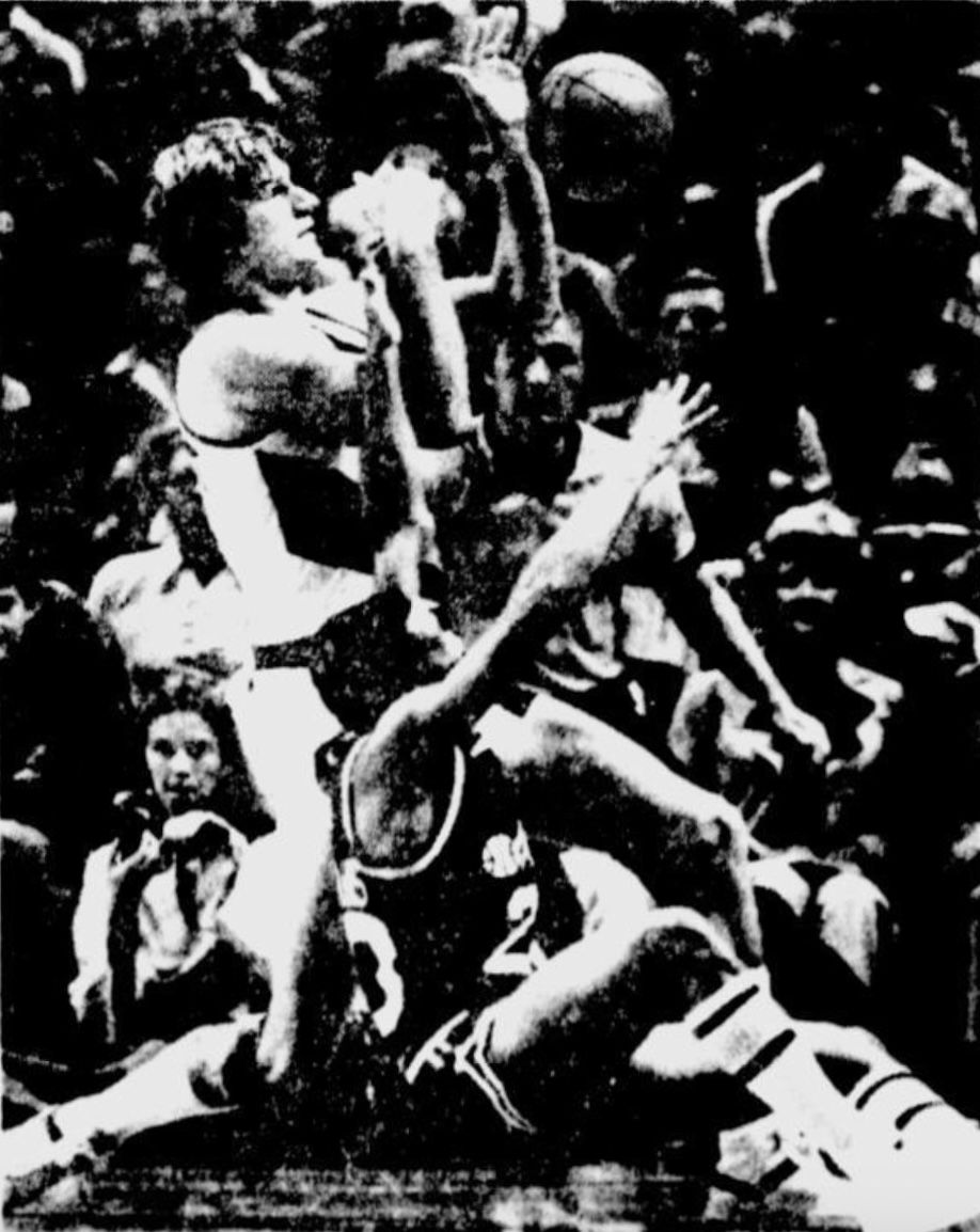 An old newspaper photo of two men playing basketball as a crowd watches them.