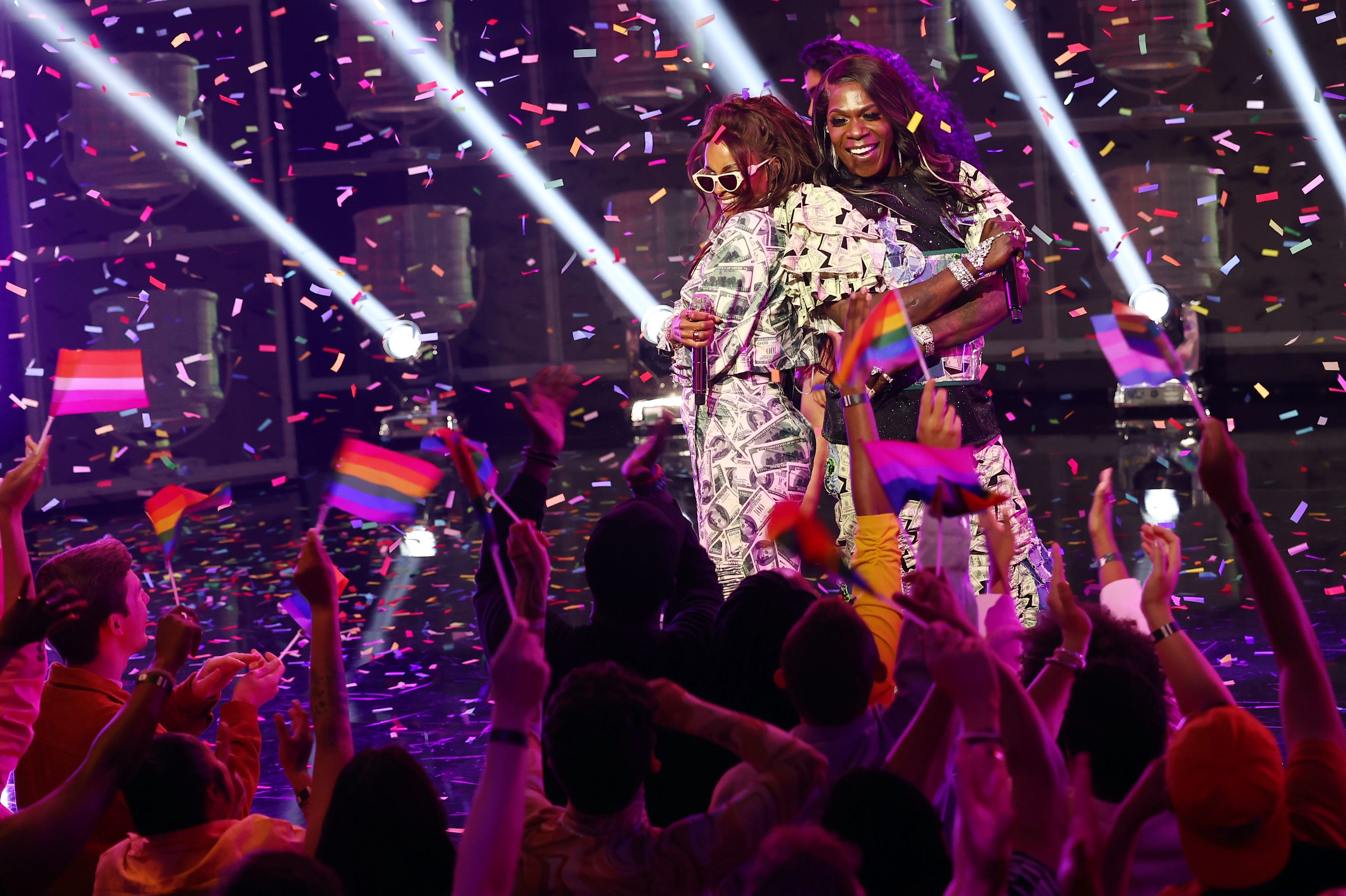 Ciara and Big Freedia pose, back to back, during an on-stage performance. Rainbow-colored confetti and spotlights fill the air around them.