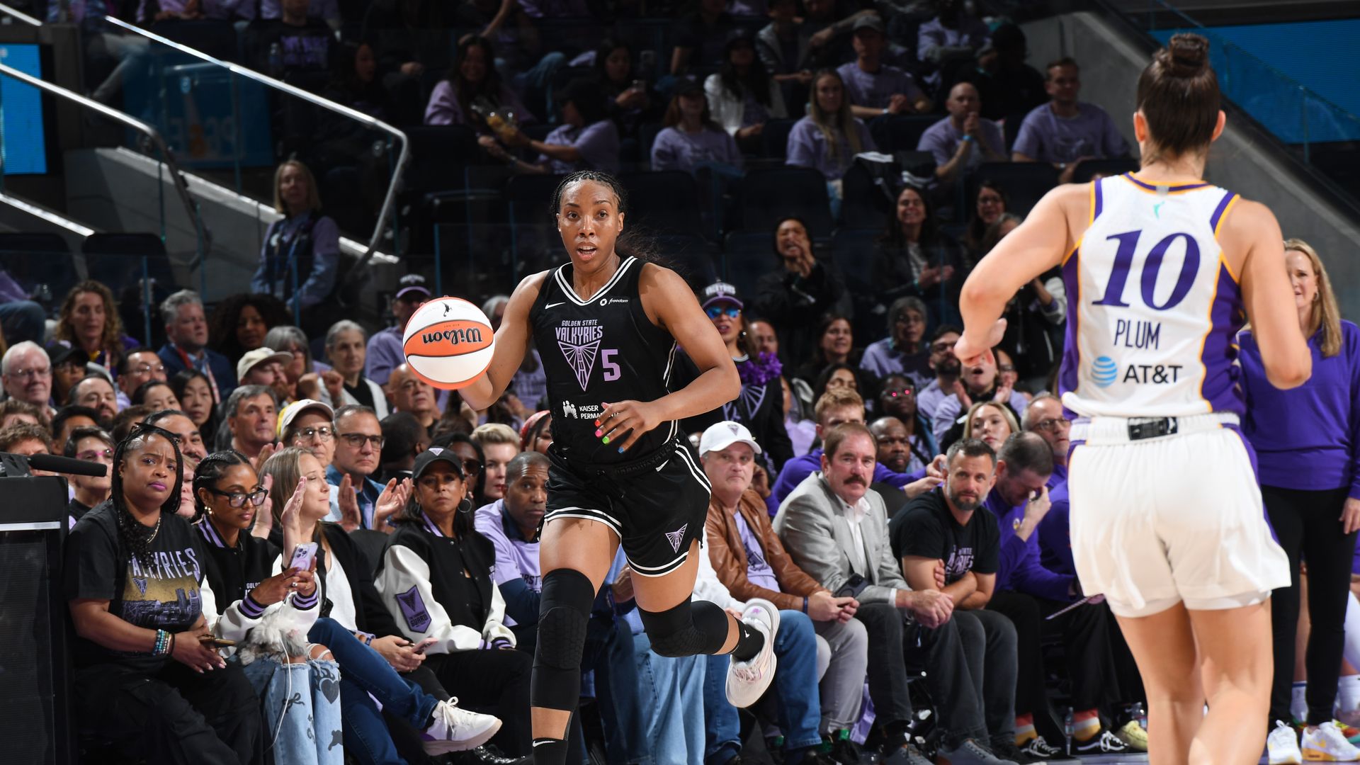 A woman in a black basketball uniform dribbles the ball
