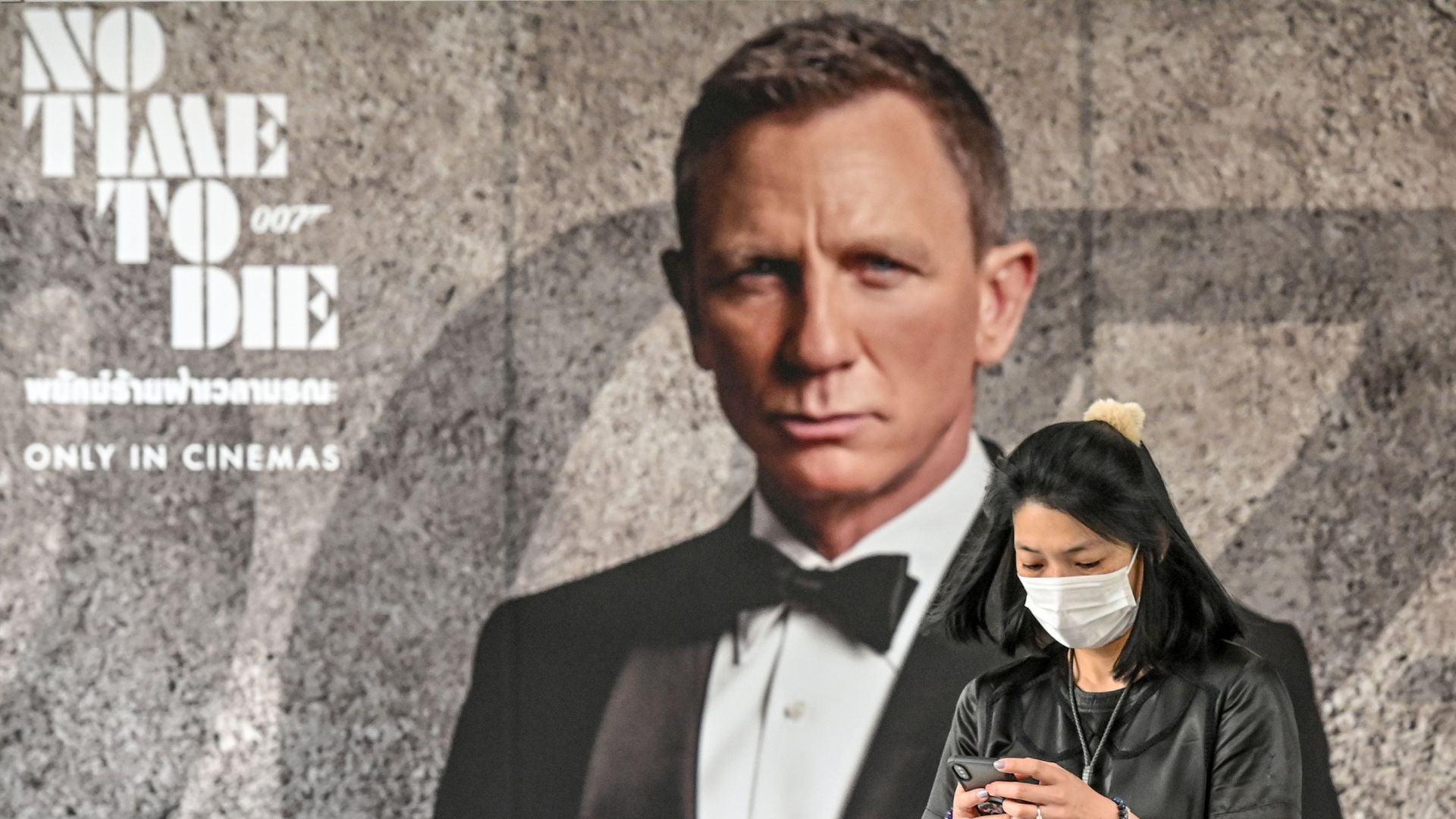 A woman wearing a face mask in front of a "No Time to Die" poster in Bangkok