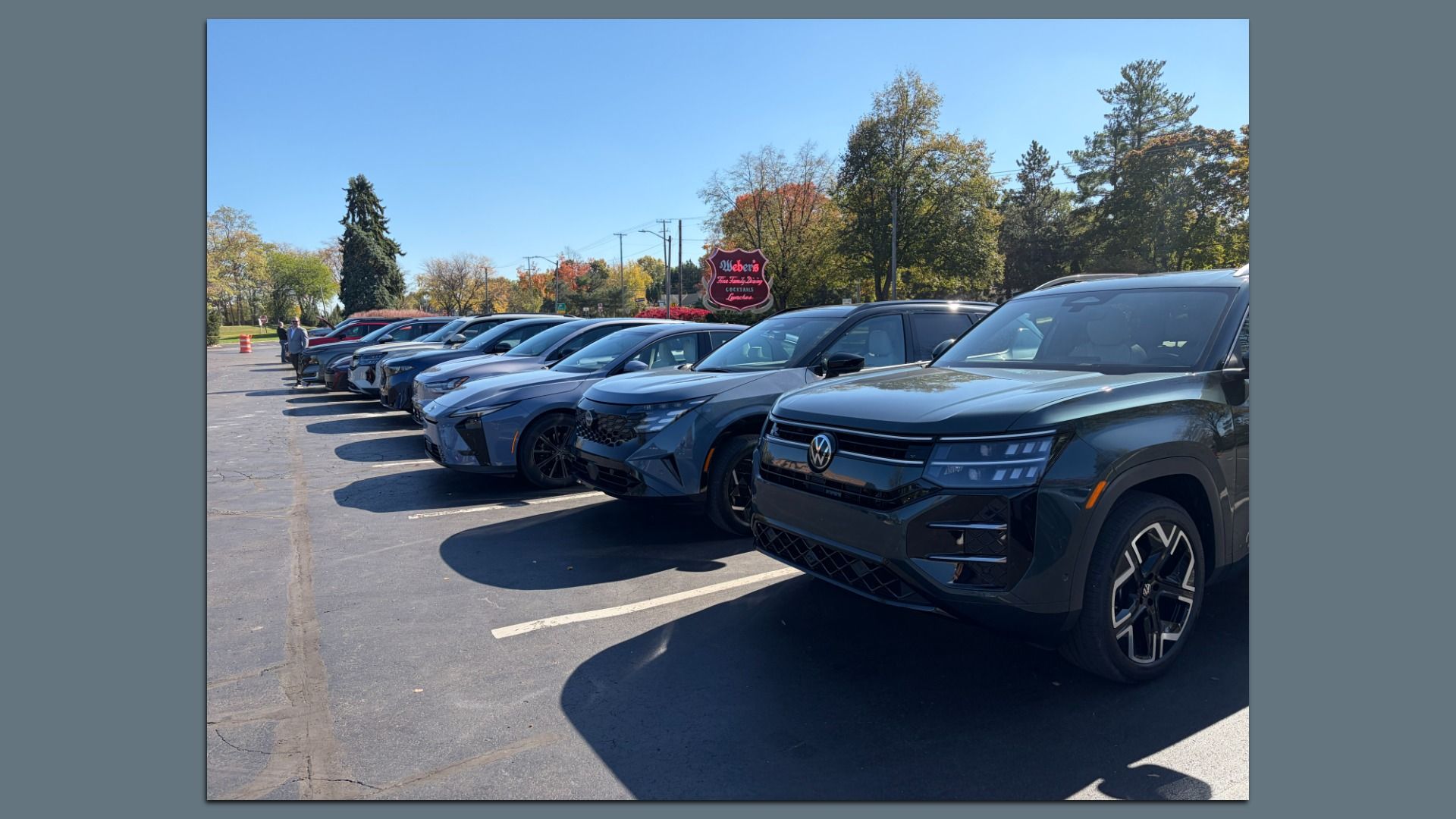 A row of parked vehicles in a sunny lot, with autumn trees and a red sign for Weber's restaurant visible in the background.