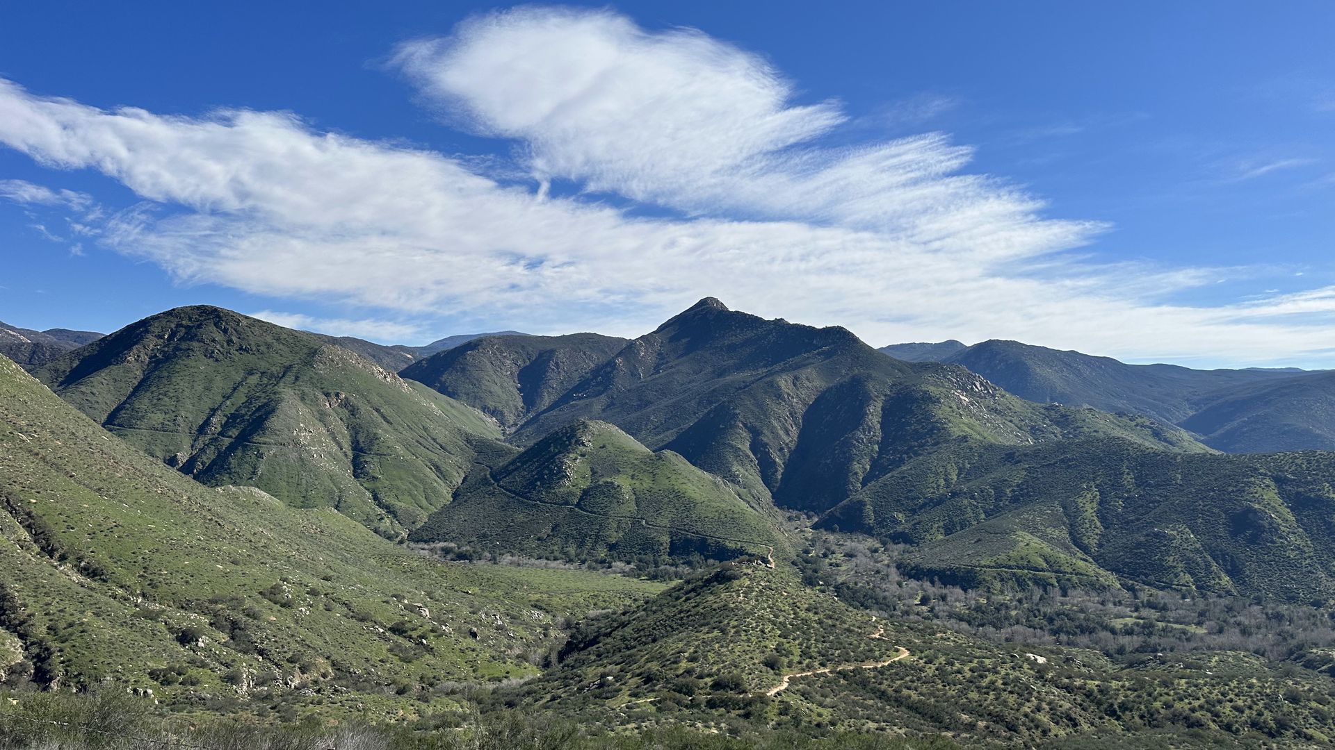 A landscape view of a trail through green mountains and a blue sky with clouds.
