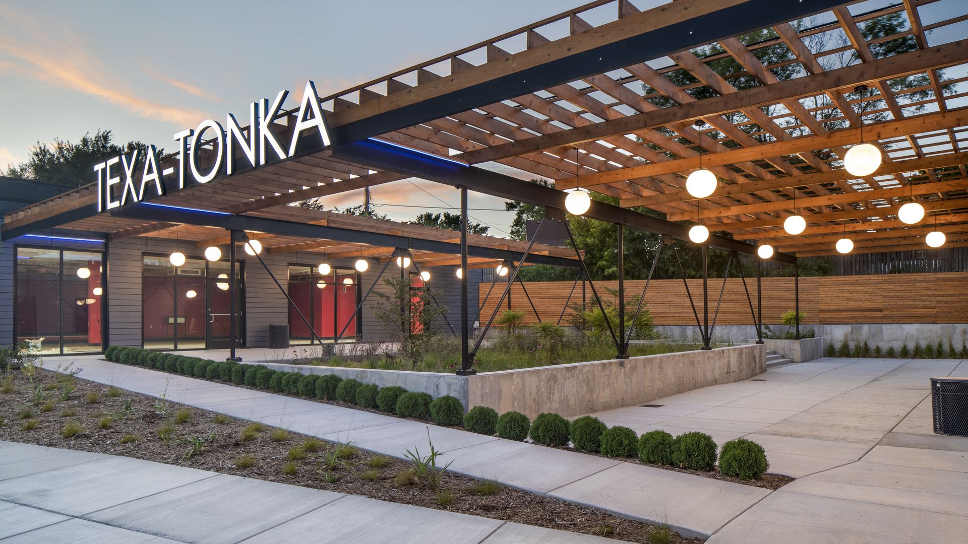 A glowing Texa Tonka sign above a new plaza with concrete and plantings 