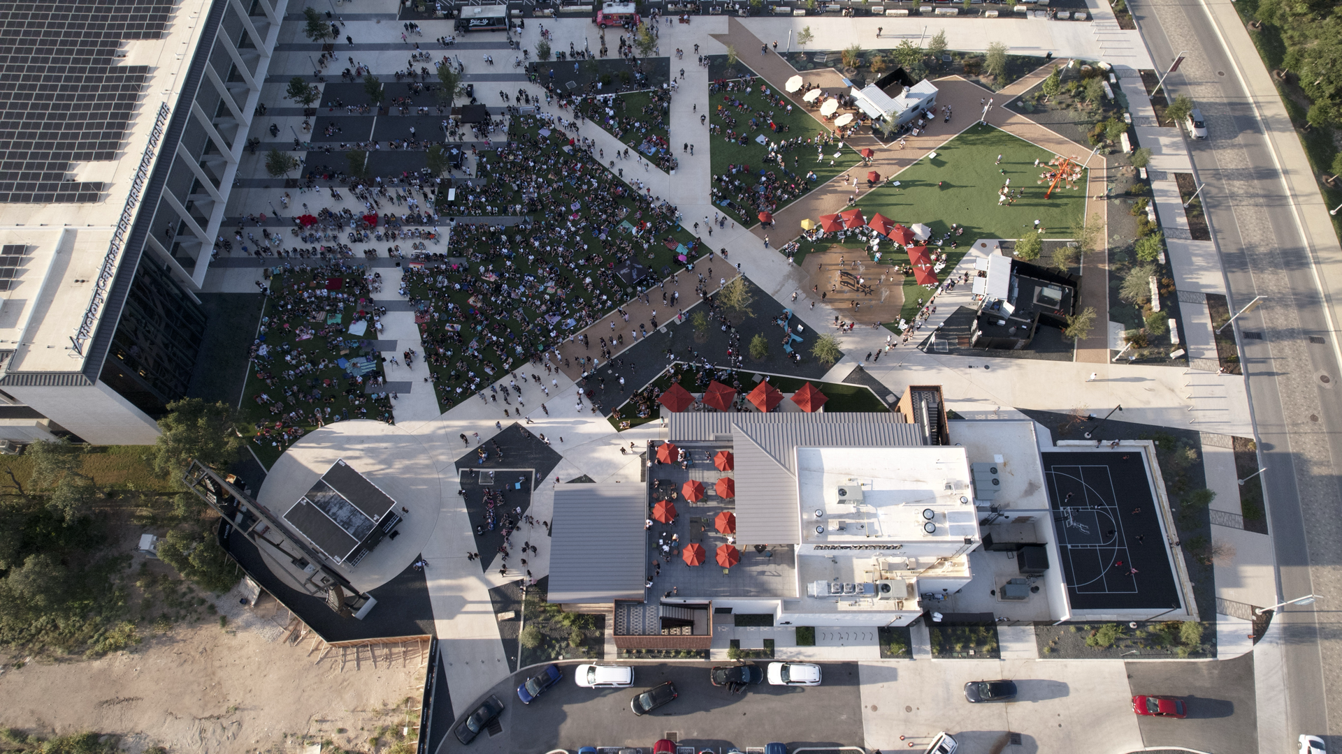 A drone view of a mixed-use property with people gathered on a green space. 