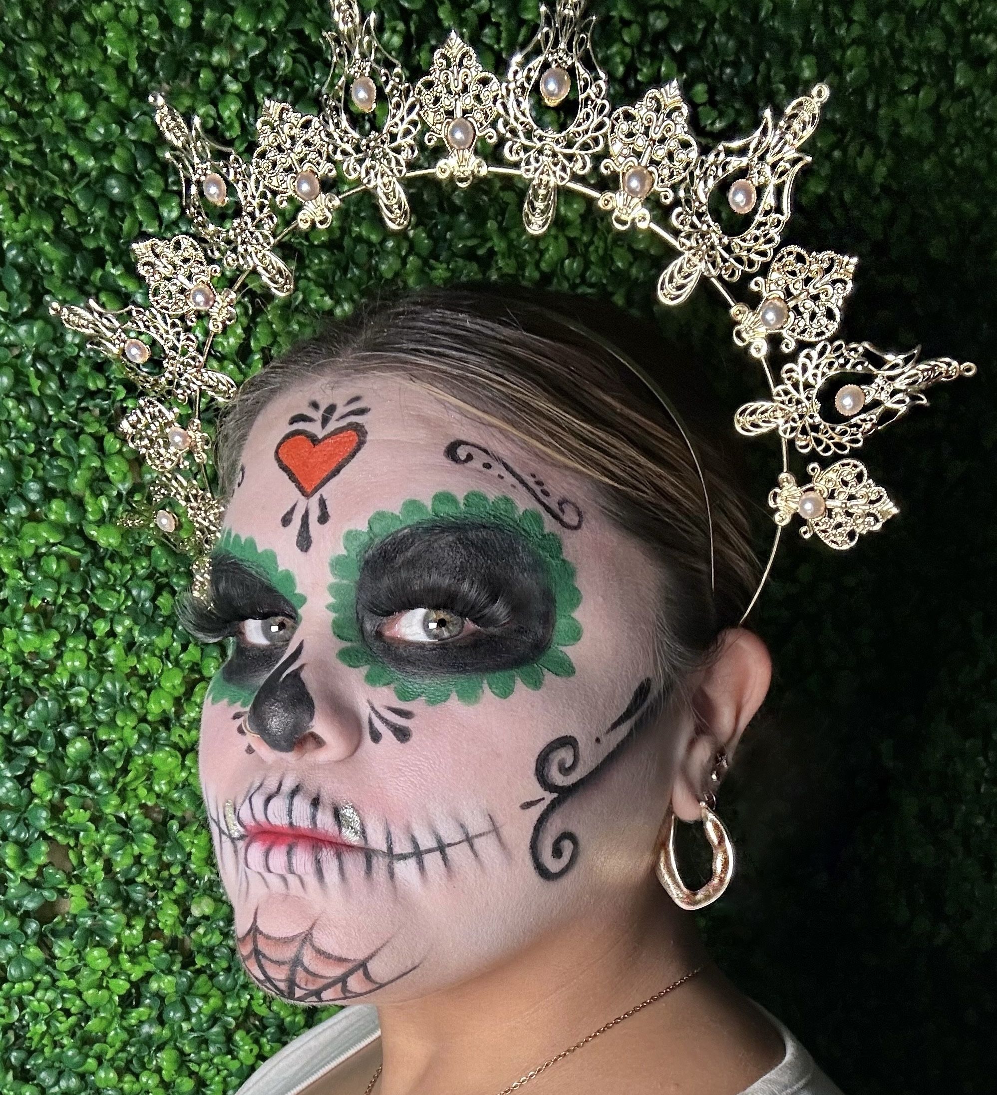 A woman wearing a crown and calavera makeup looks at the camera. 