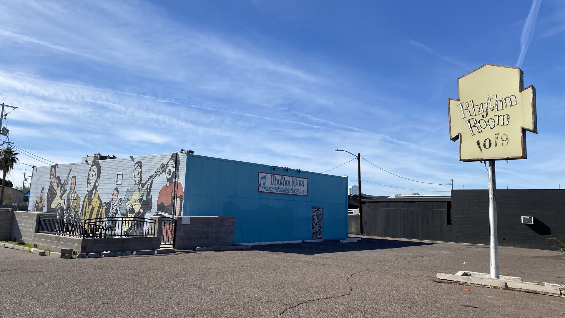 A building with a mural of musicians on one side next to a sign that reads Rhythm Room.