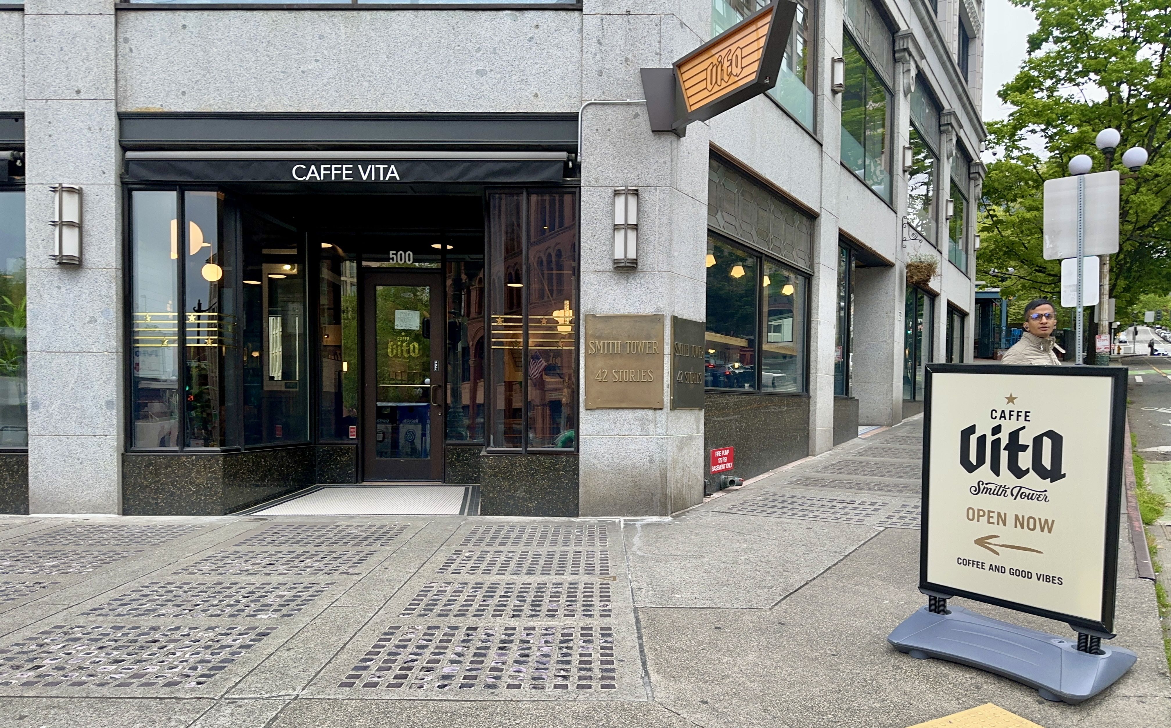 The outside of the Caffe Vita in Smith Tower, with a sign on the sidewalk that says "Caffe Vita" with an arrow.