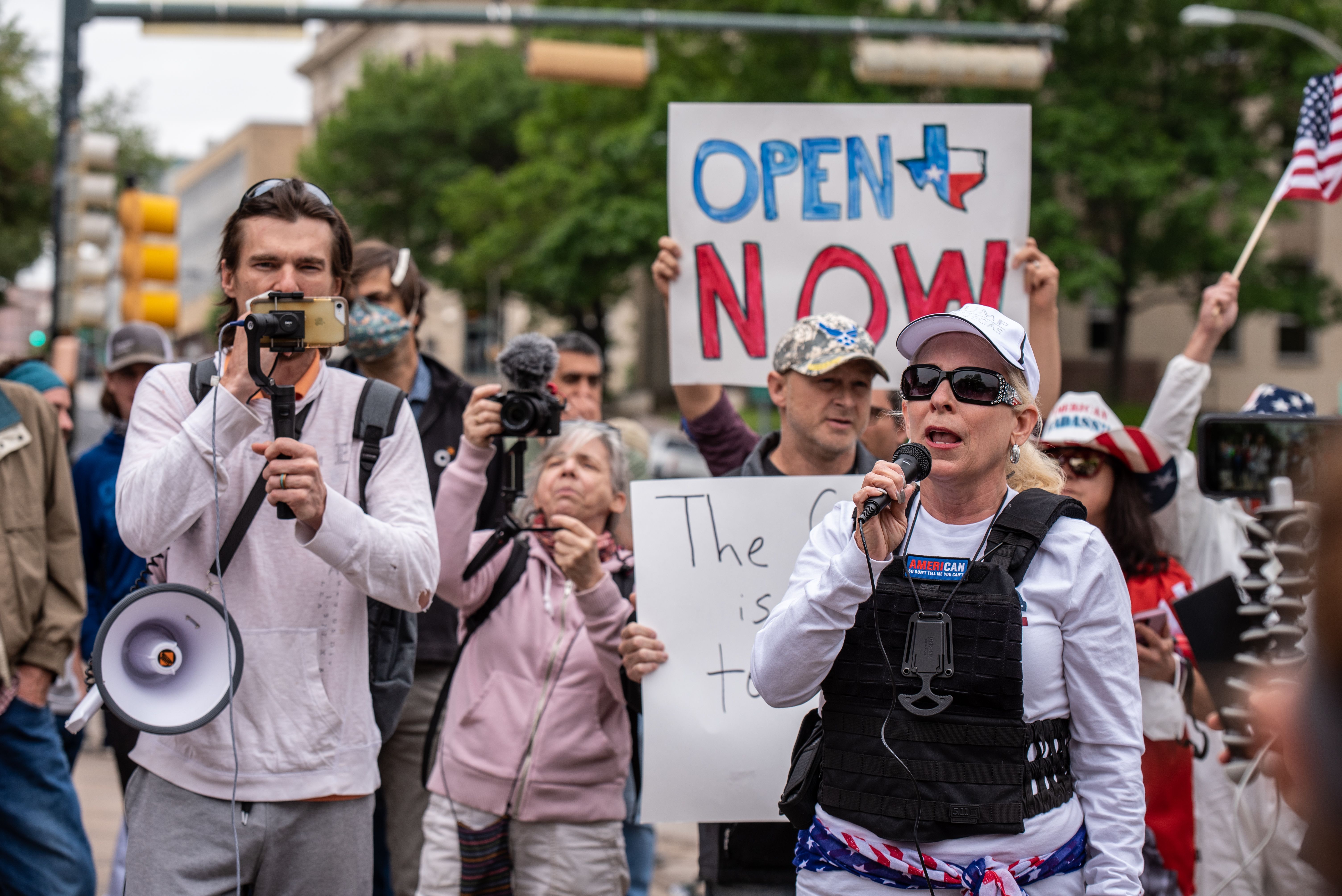 In this image, a woman speaks into a microphone while a sign behind her reads "Open texas now"