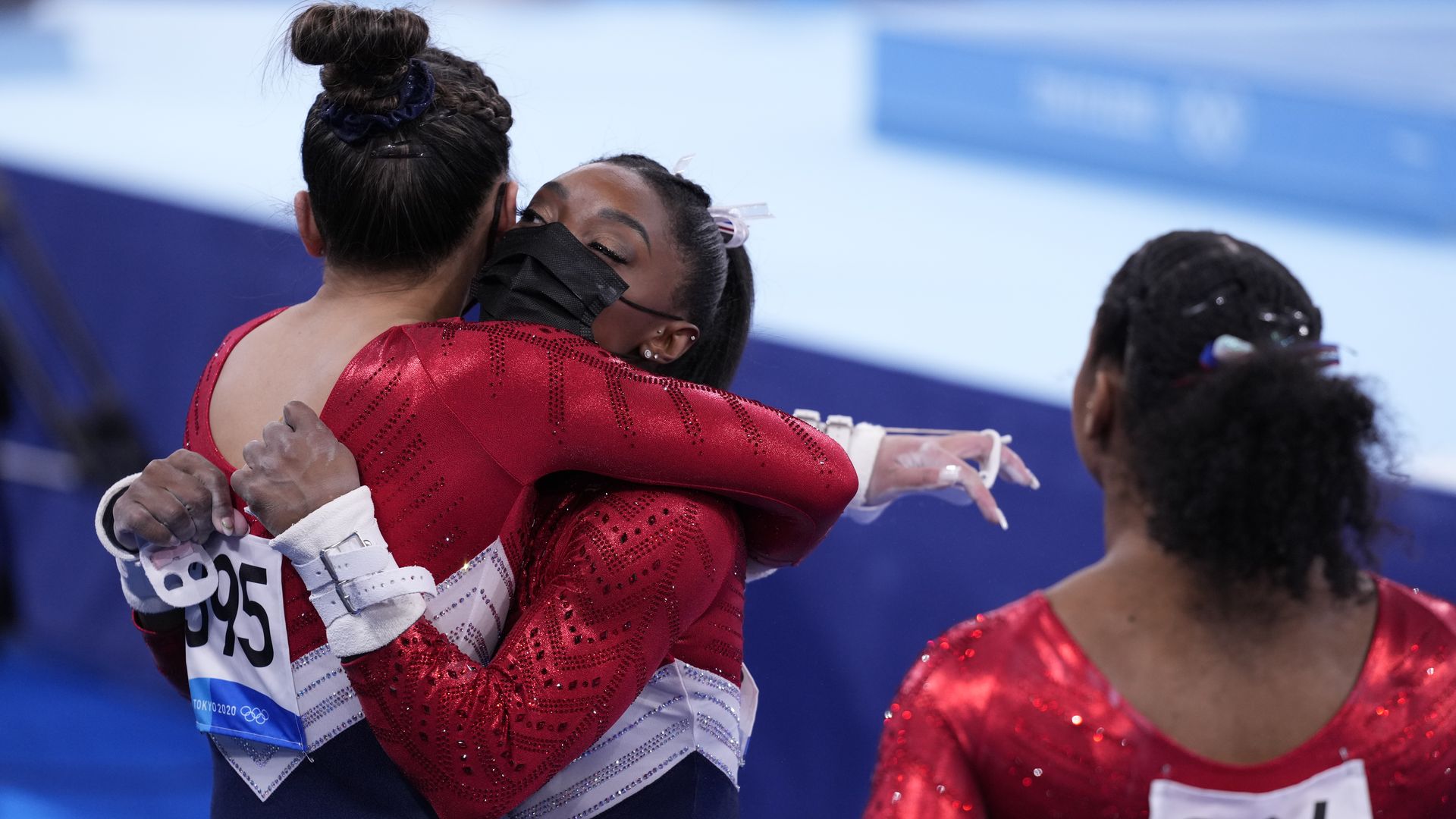 Photo of a masked Simone Biles in her gymnastics uniform hugging a fellow teammate