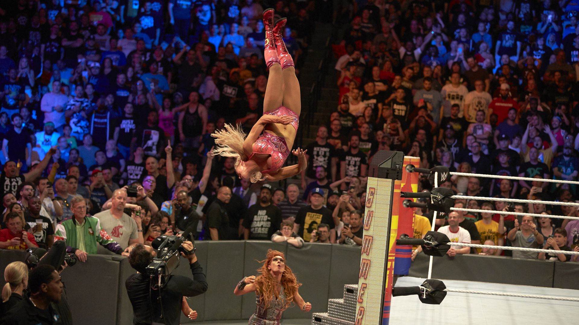 A wrestler twirls vertically in the air as spectators watch.