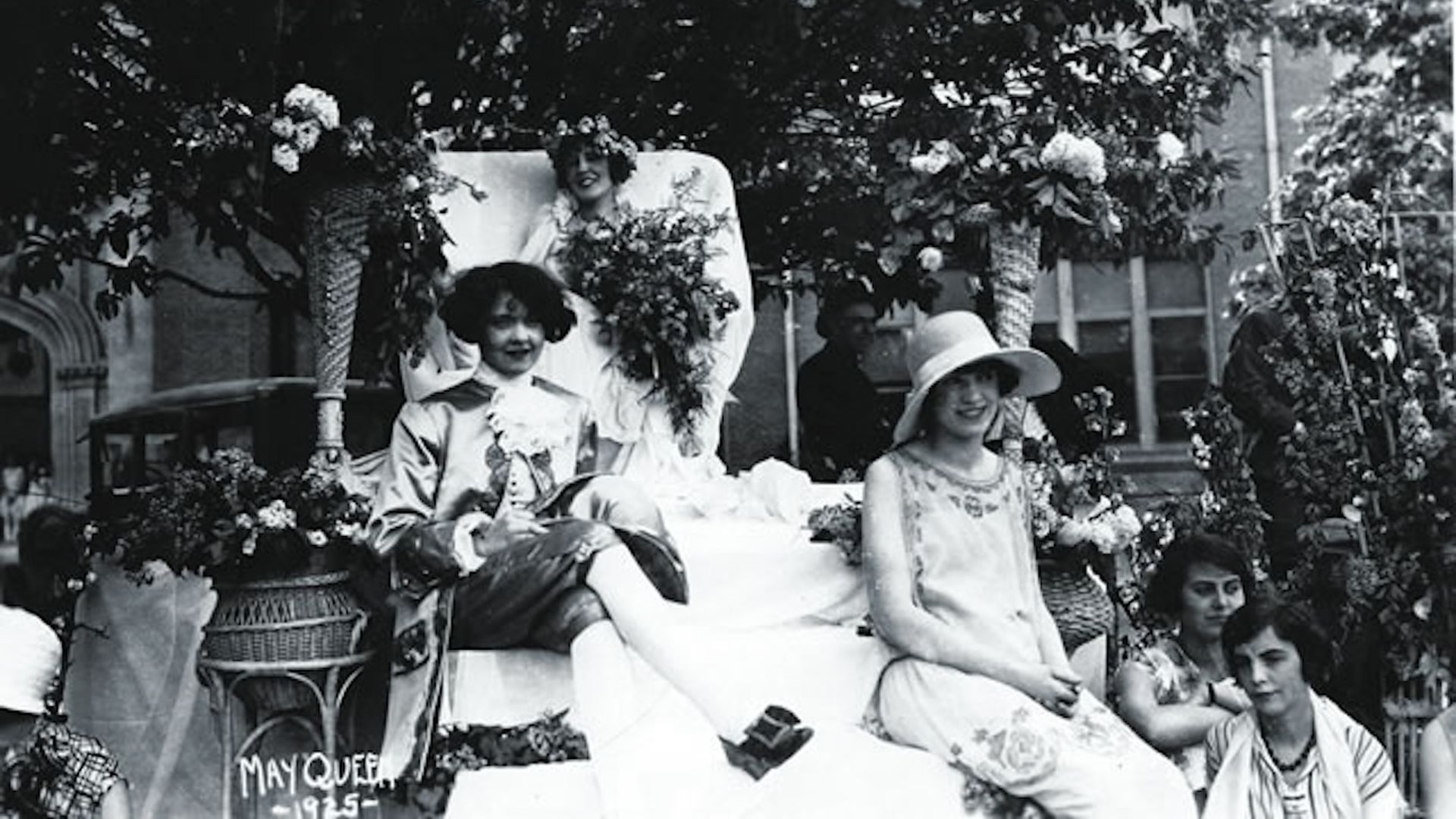 Three women ride in a parade float in summer dresses in a 1925 photo.