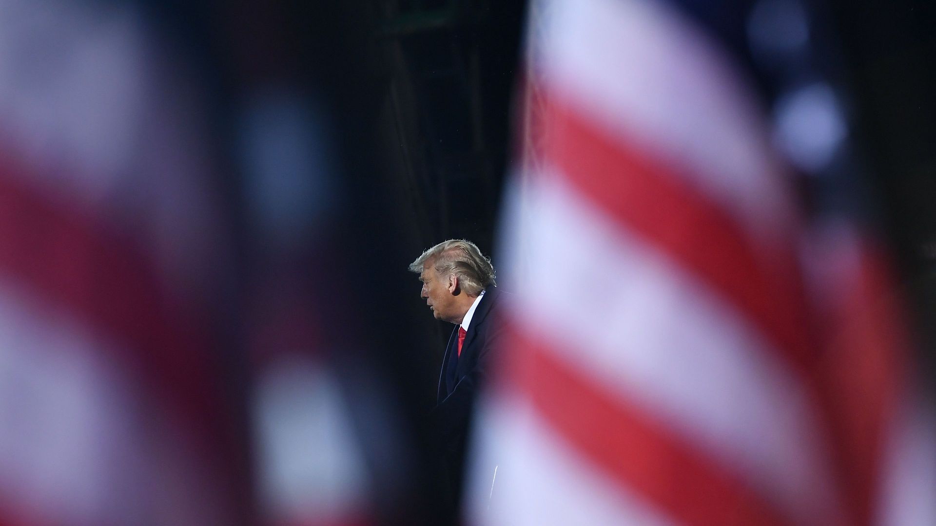 Donald Trump speaking at a podium, seen between two blurred American flags